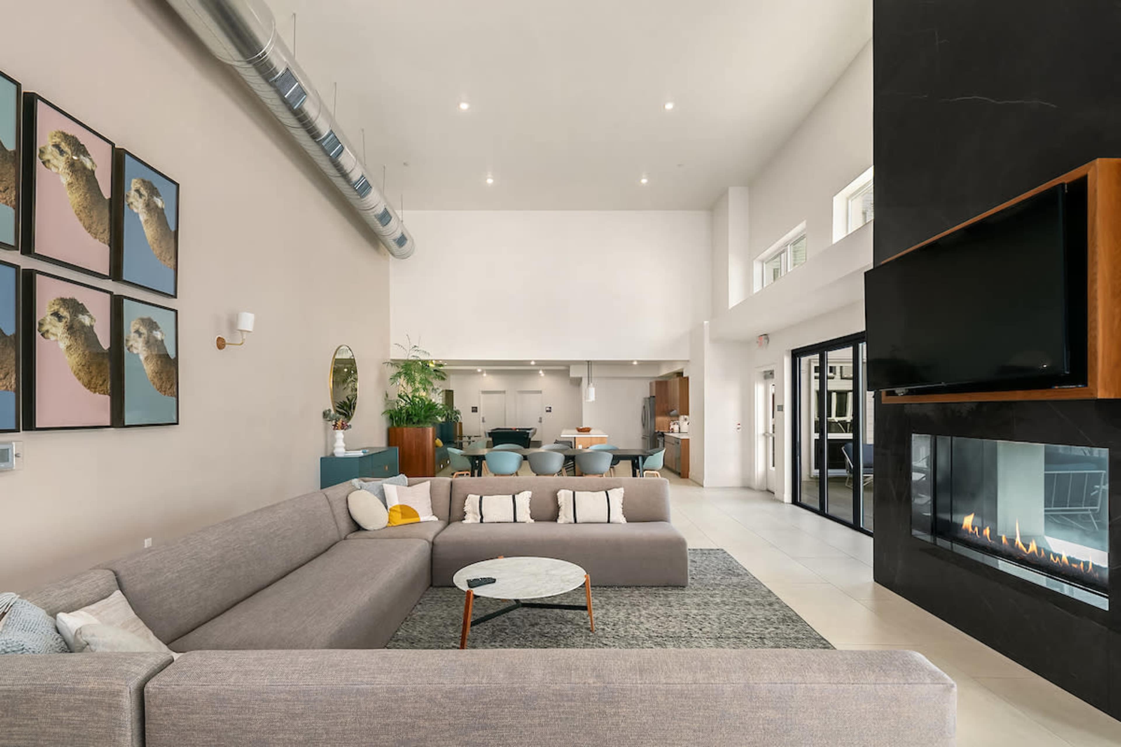 The image depicts a modern living space with a large sectional sofa, a circular coffee table, and a wall-mounted television above a linear fireplace.