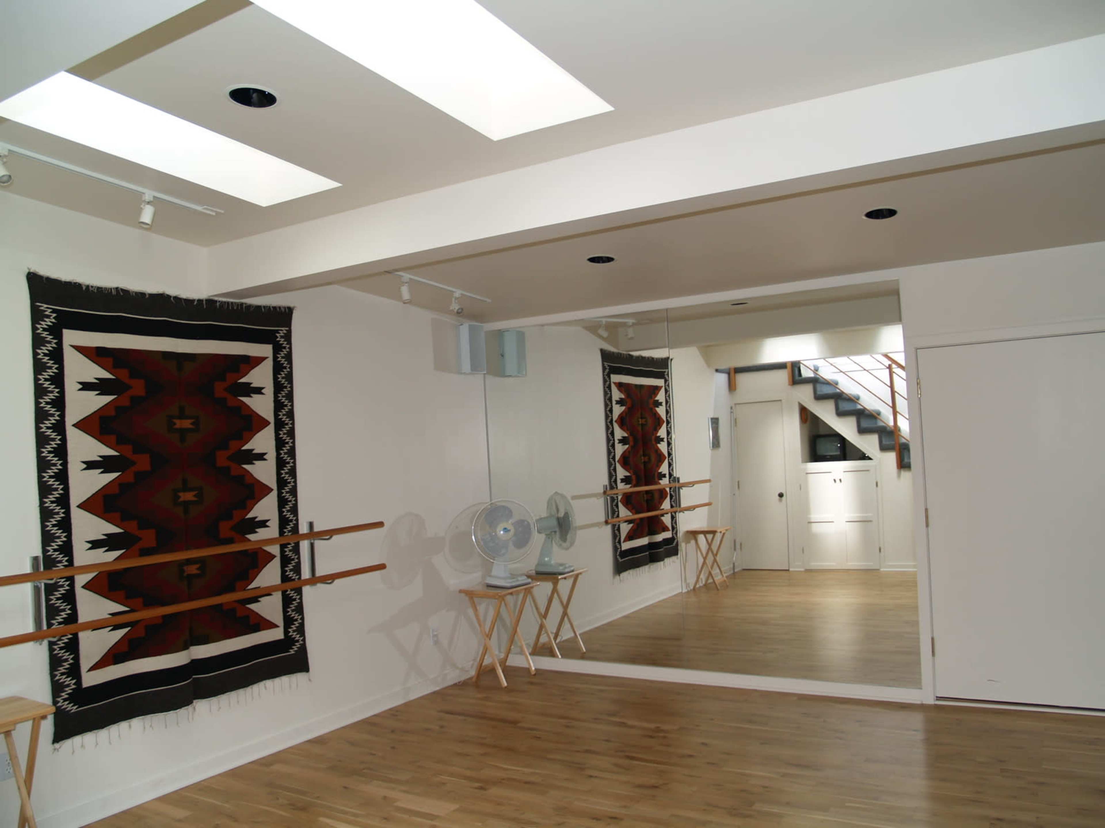 A dance studio featuring hardwood floors, a mirrored wall, barres, and decorative rugs displayed on the walls.