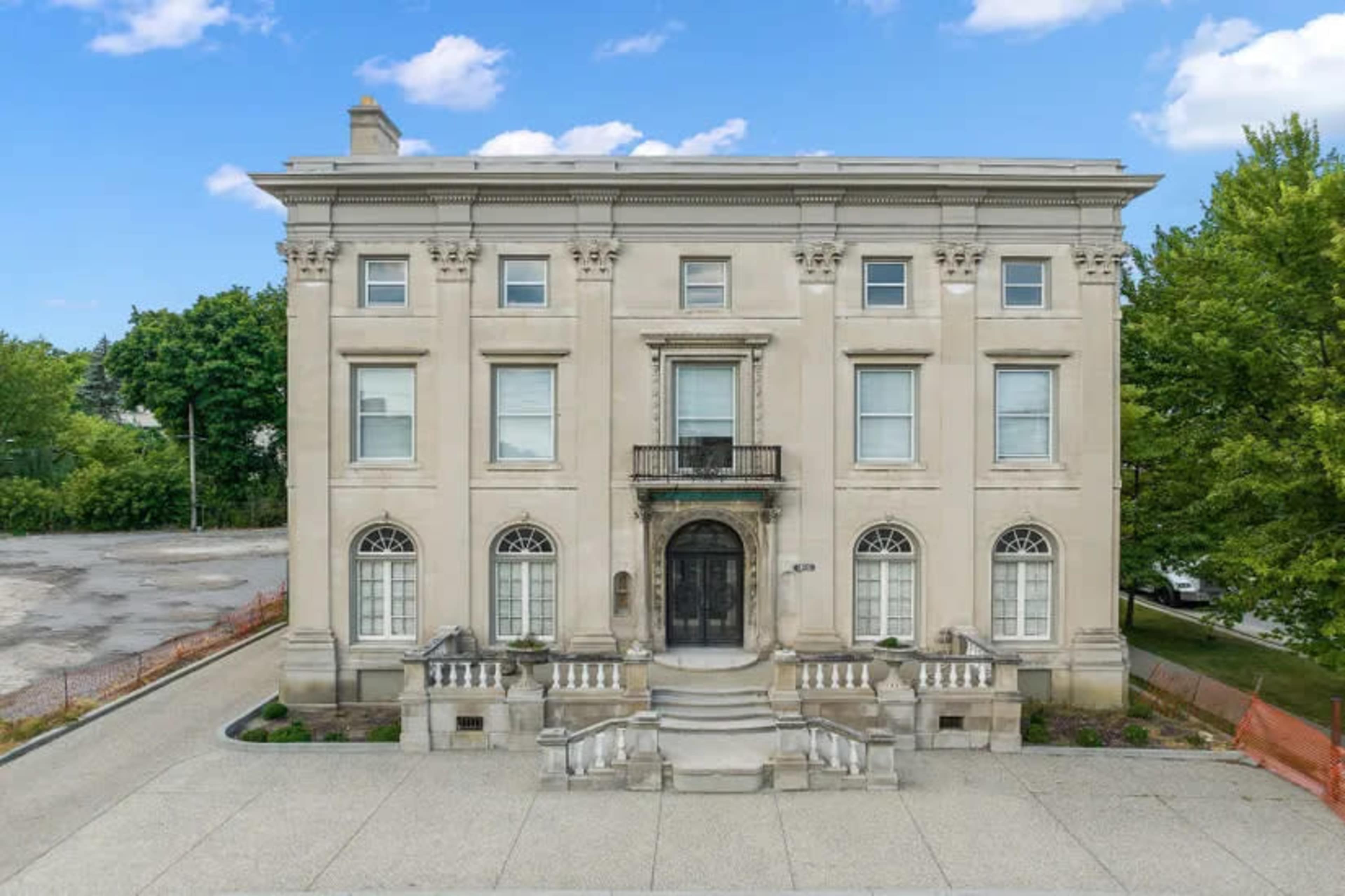 The image shows a large, stately building with a symmetrical facade, featuring arched windows and a central entrance framed by steps and a balcony.