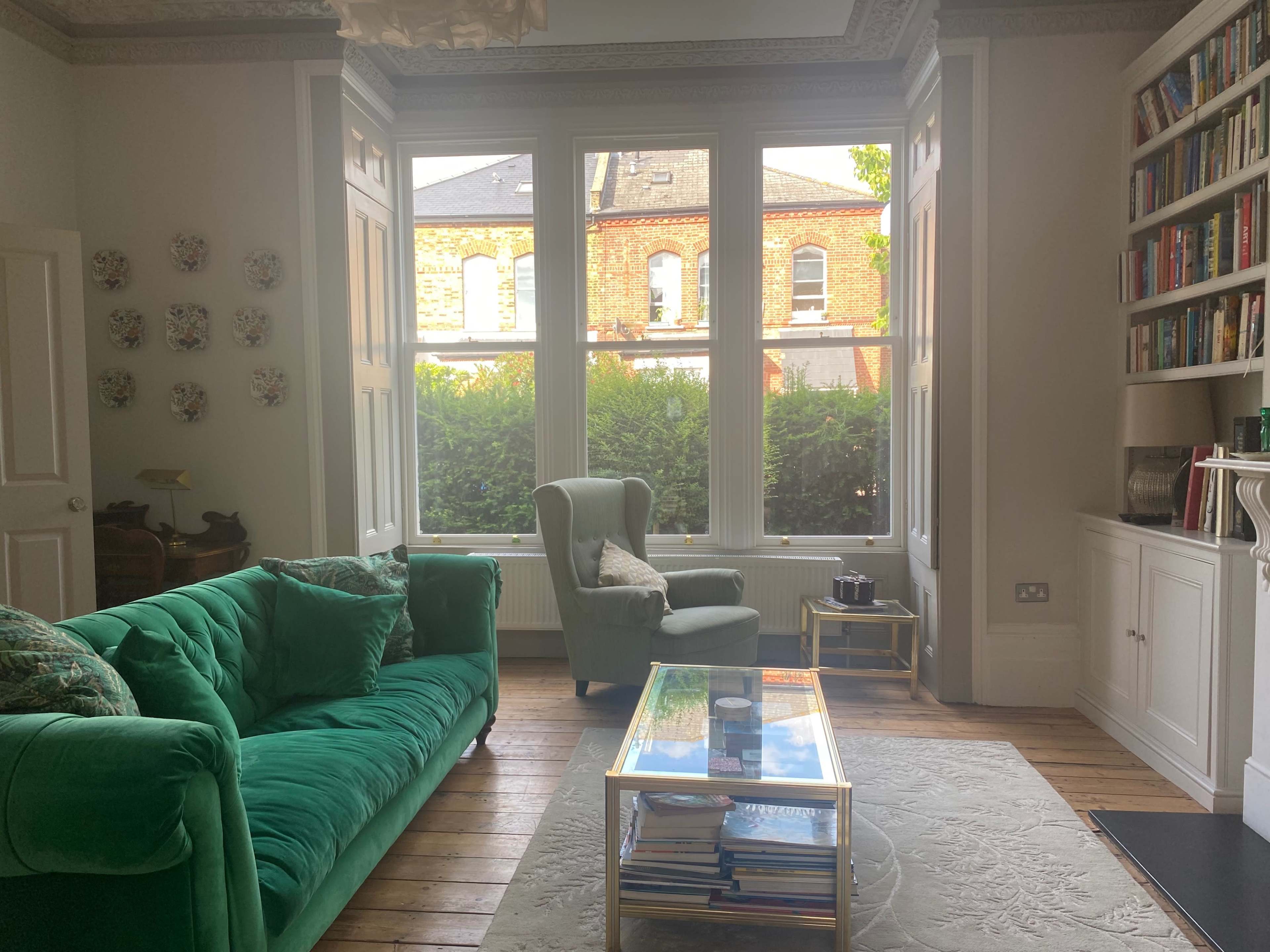 A bright living room with a green sofa, a glass coffee table, and large windows overlooking a garden.