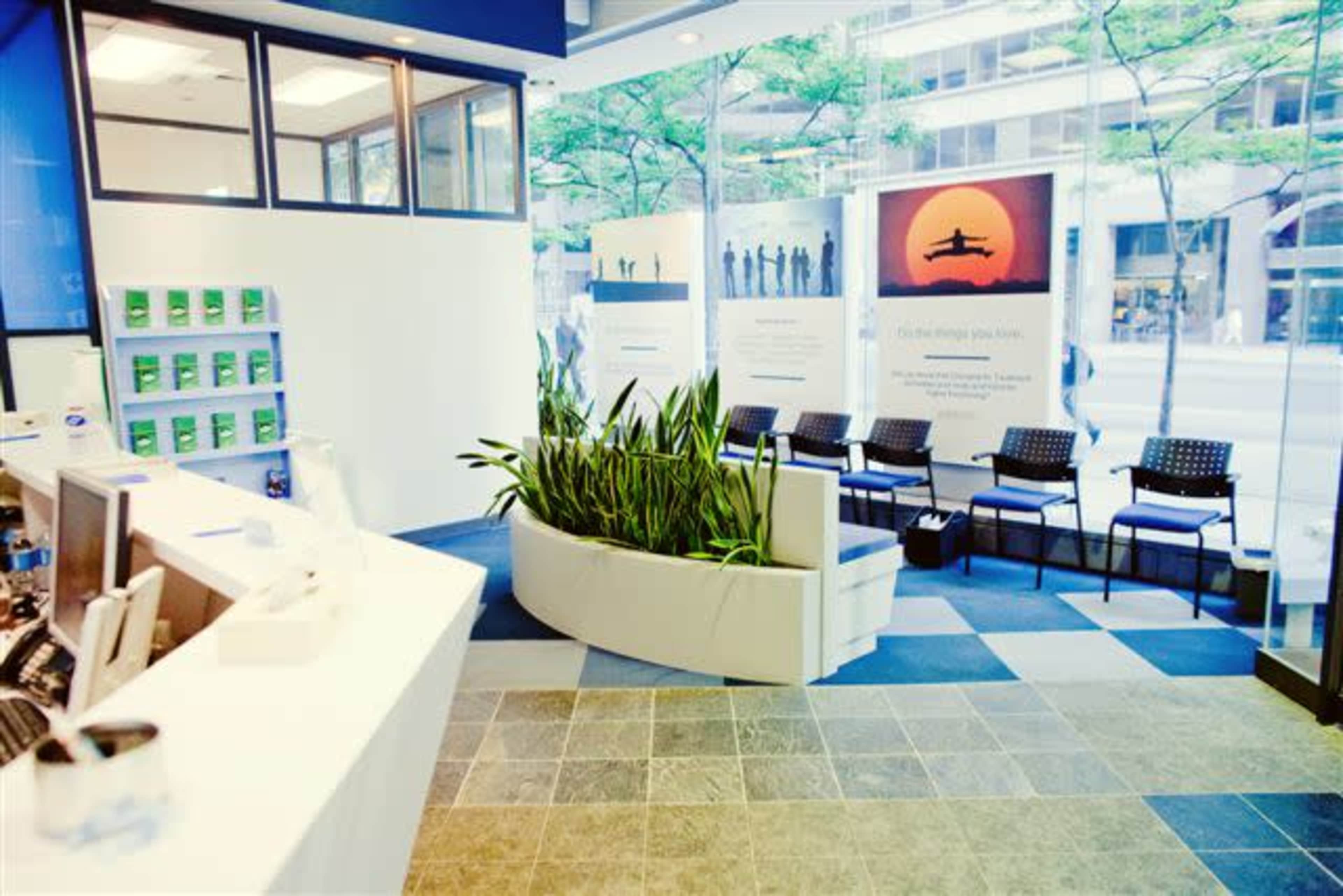 A modern reception area with a front desk, several chairs for waiting guests, and large windows that provide natural light and views of the outside.