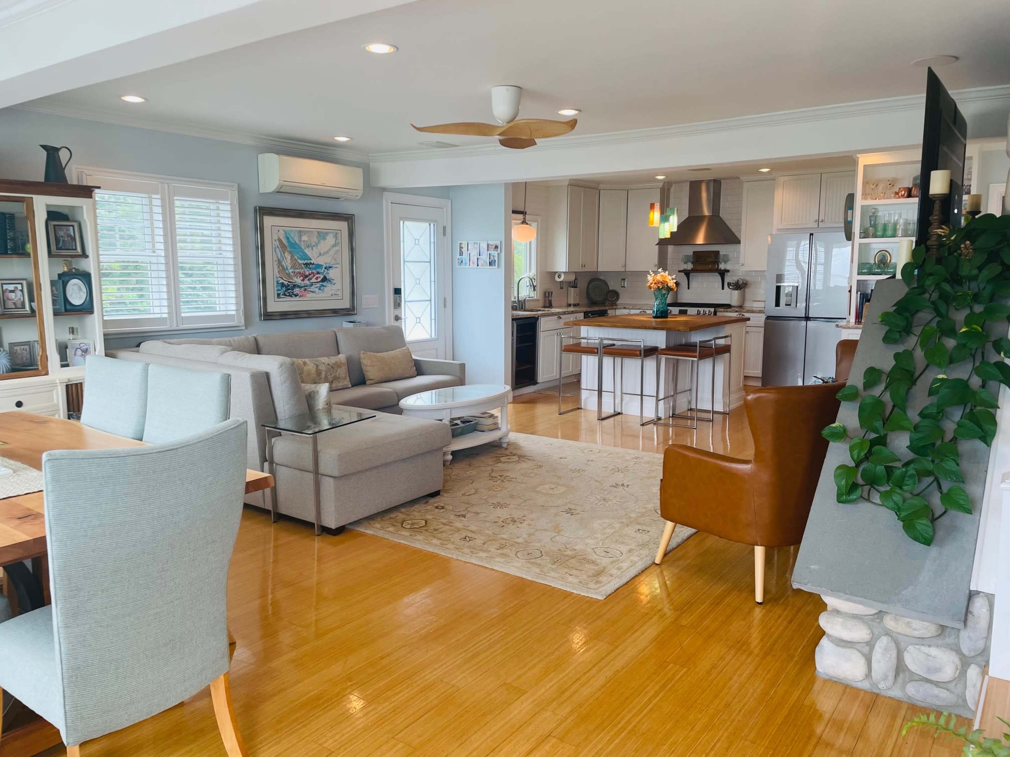 A modern living room and dining area feature light-colored furniture, a wooden dining table, and a large kitchen island, creating an open-concept design.