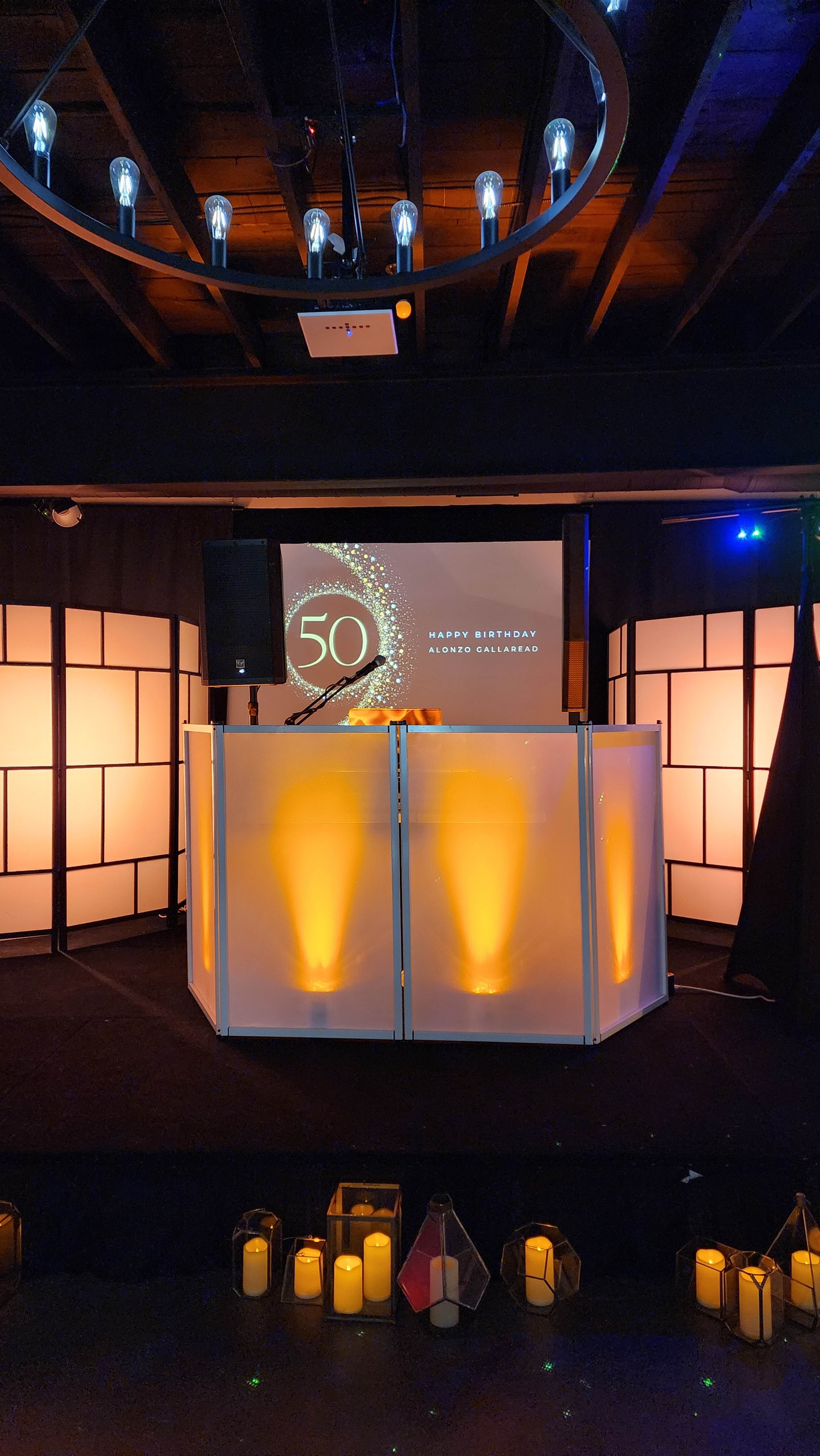 A decorated stage with illuminated partitions displays a "50" sign, set against a backdrop featuring a celebratory message for a birthday event.