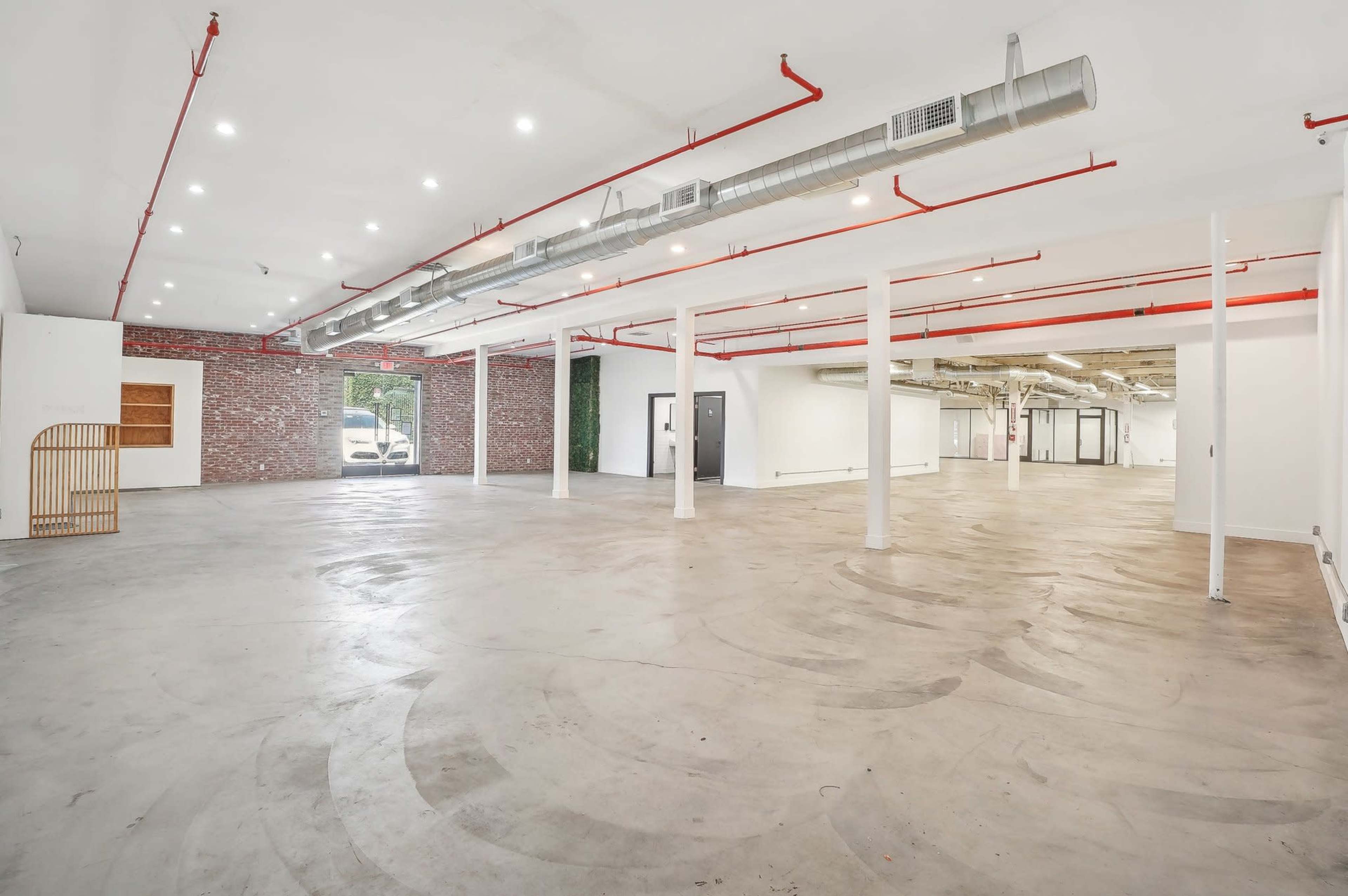 The image shows a spacious, empty commercial interior with exposed brick walls and industrial-style light fixtures.