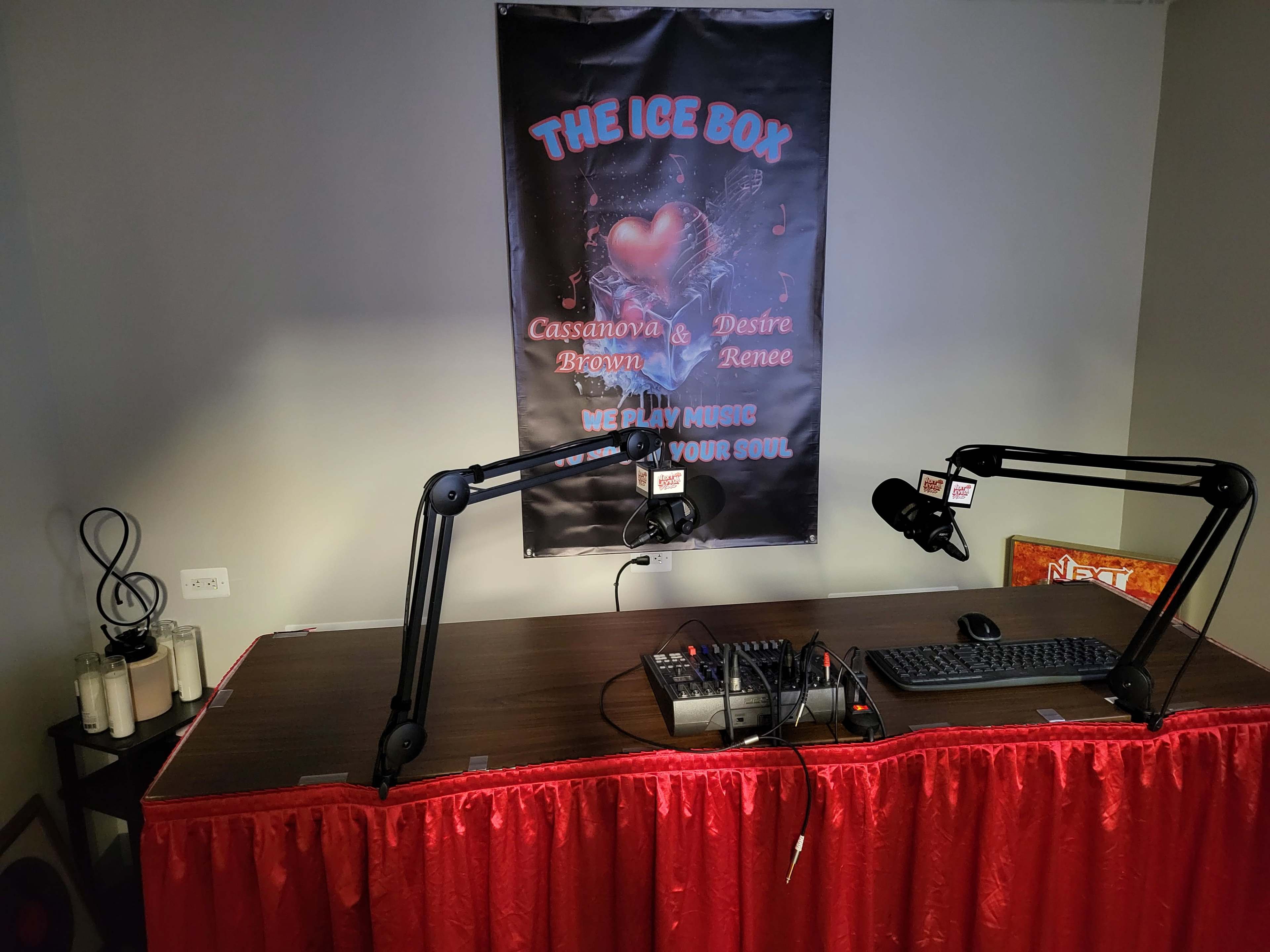 The image shows a radio broadcasting setup with a wooden table, microphone arms, a soundboard, and a red curtain, framed by a banner that reads "THE ICE BOX" along with other text.