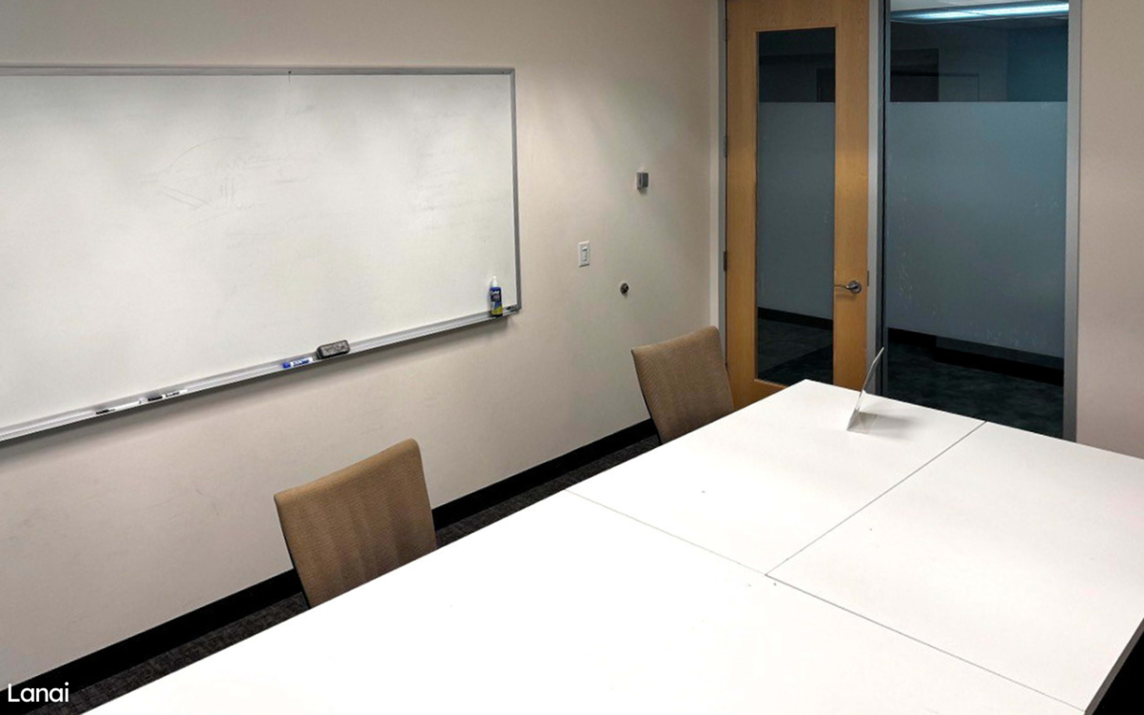A modern conference room with a whiteboard on one wall and a large table surrounded by four chairs.