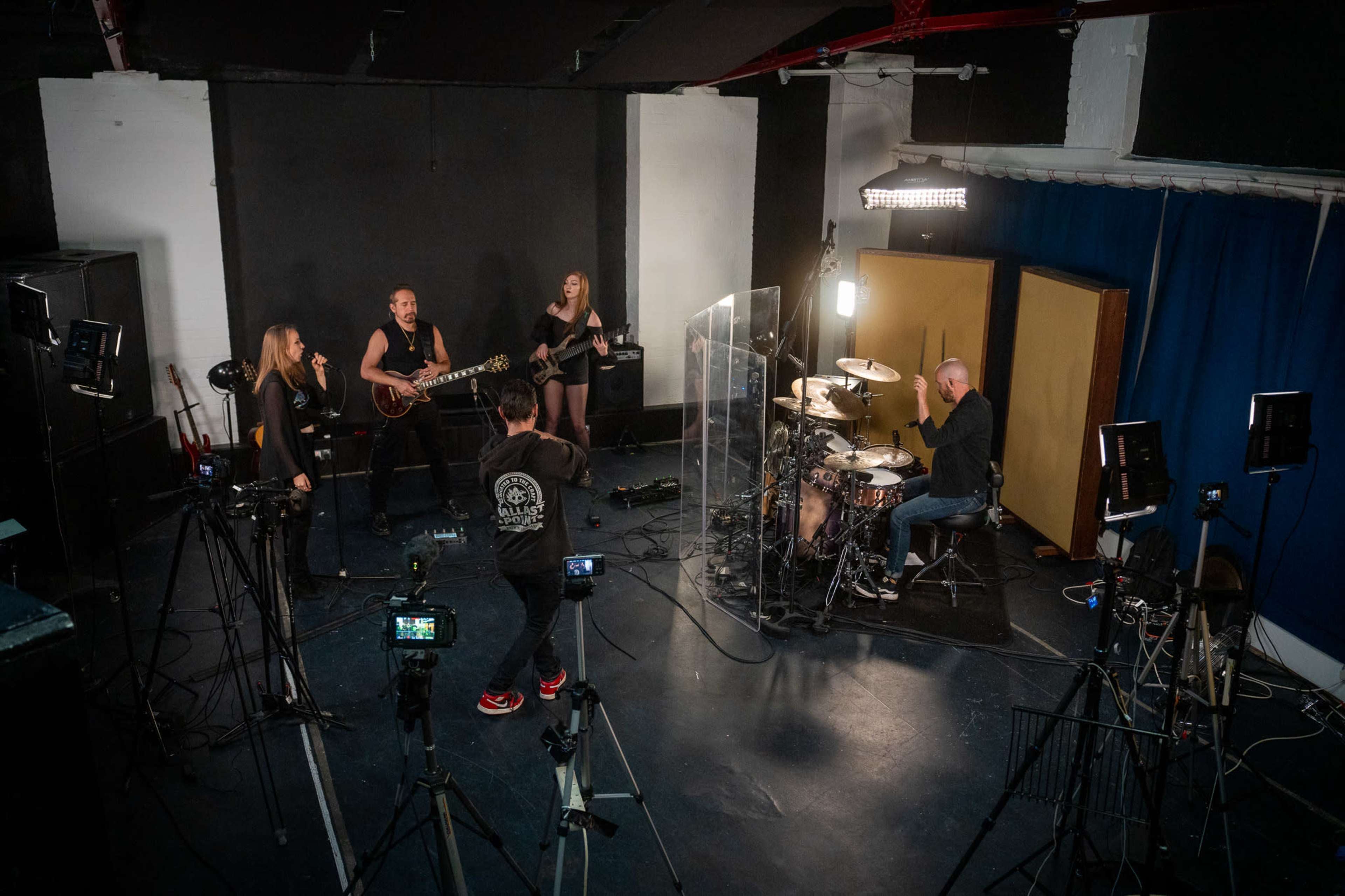 A band performs in a studio setting with multiple cameras and equipment capturing the session.