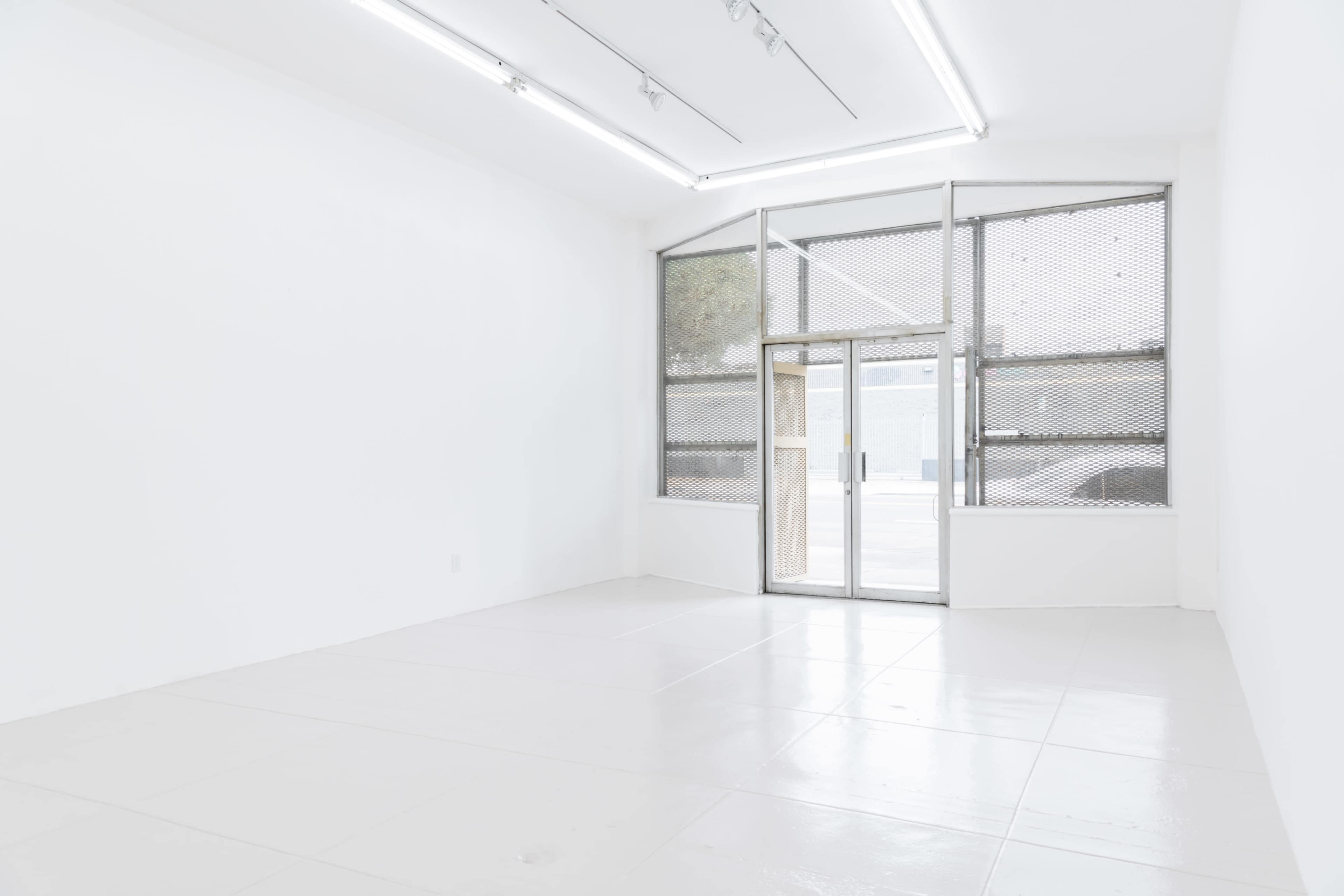 The image shows a spacious, empty room with white walls and a large glass entrance door facing a street.