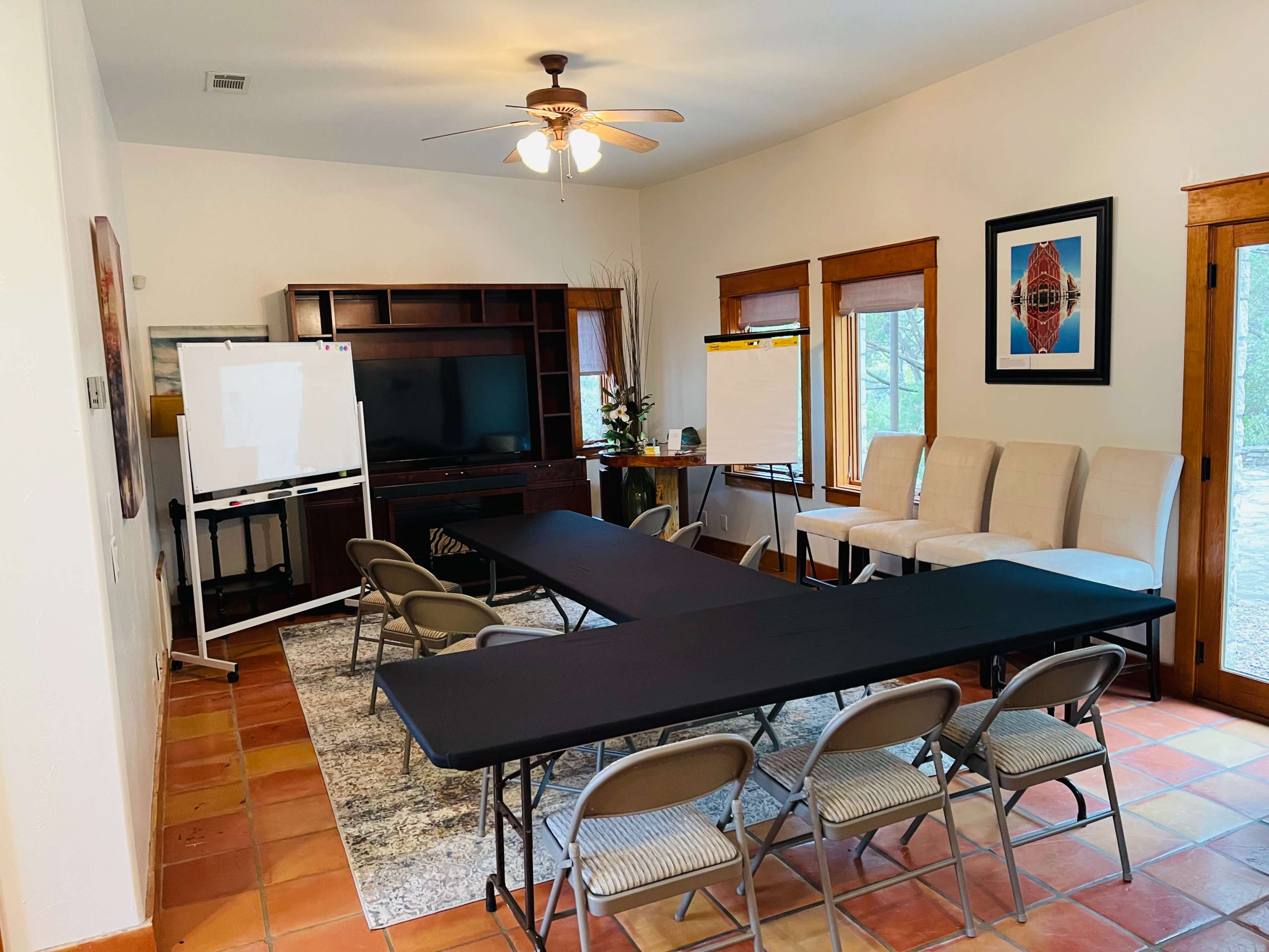 The scene shows a meeting room equipped with a long black table, six folding chairs, a large television, a whiteboard, and two flip charts.