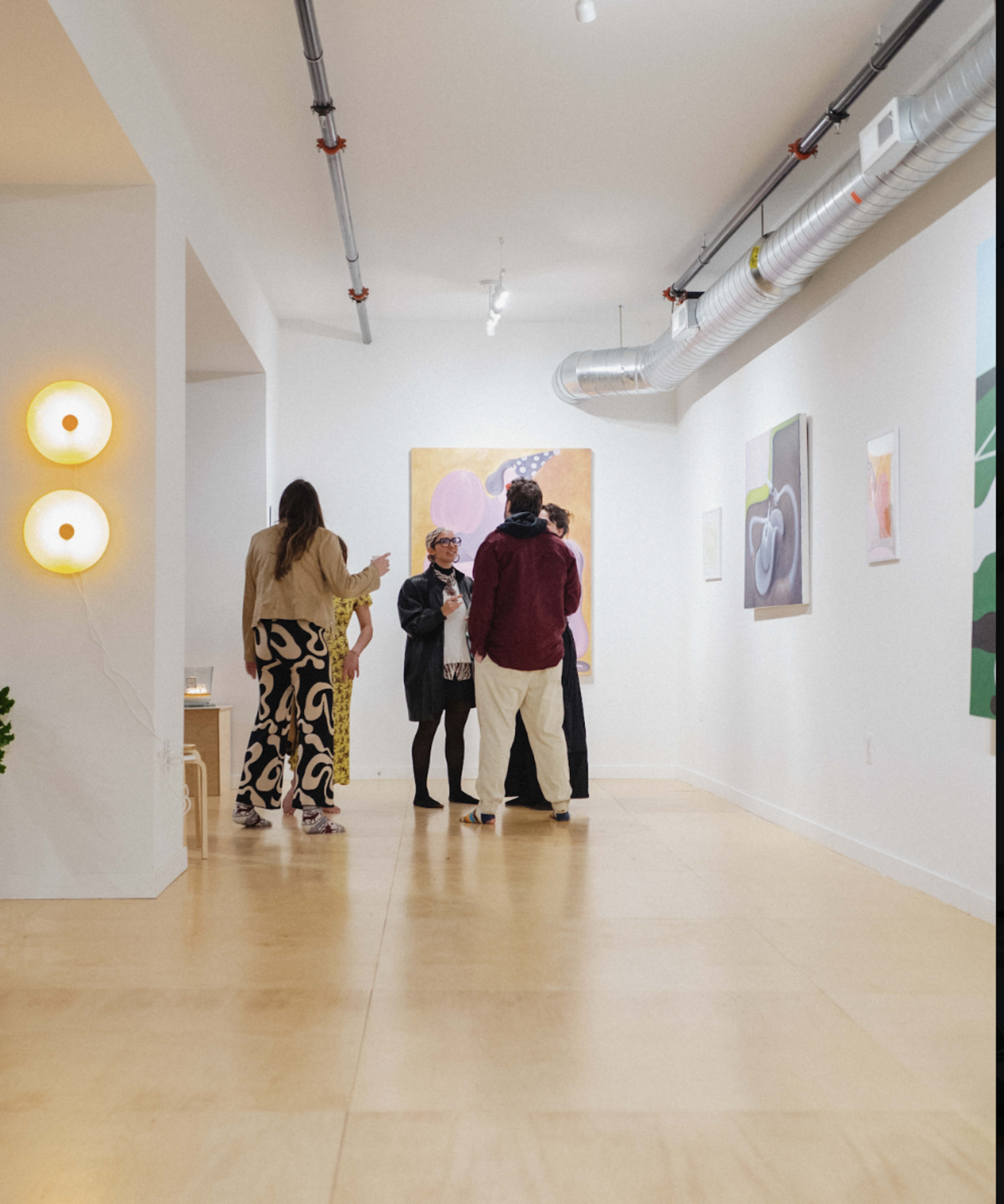 A group of people engages in conversation in an art gallery featuring colorful paintings on the walls.