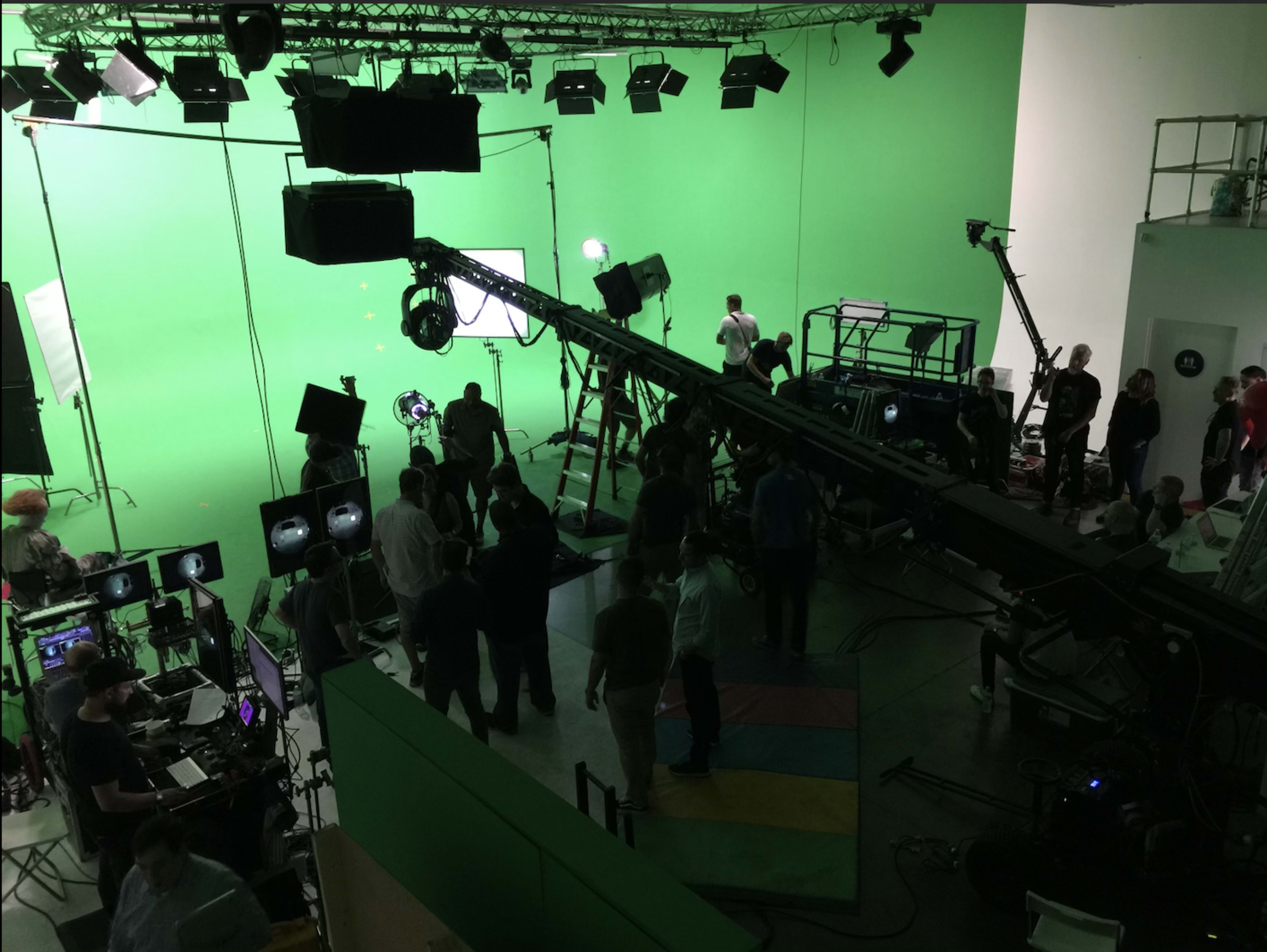 A film crew sets up equipment on a green screen stage, with various lights and cameras in use.