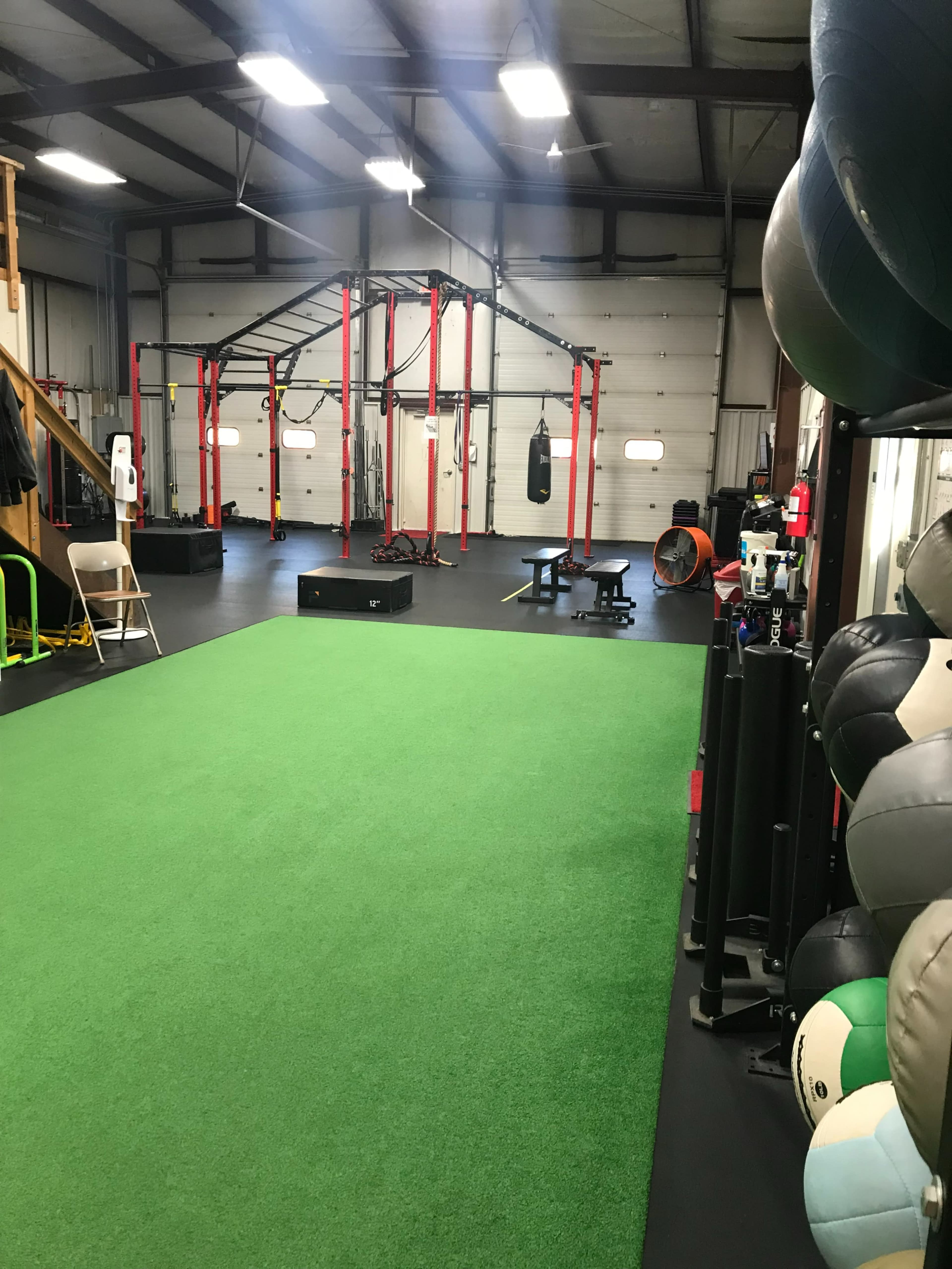 An indoor gym with a turf area, exercise equipment, a boxing bag, and various fitness apparatus arranged on black flooring.