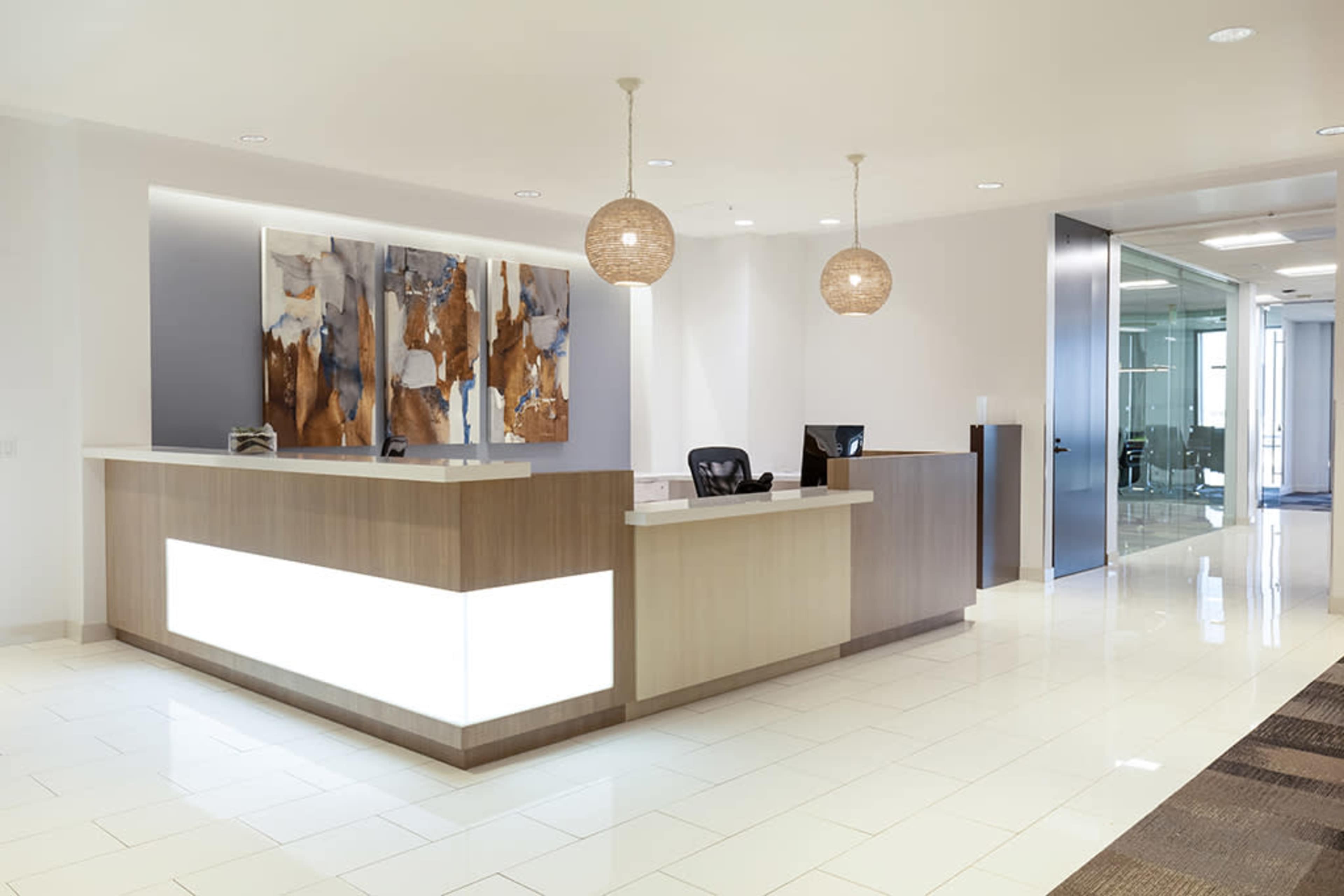 A modern reception area features a sleek front desk with decorative lighting and abstract art on the walls.