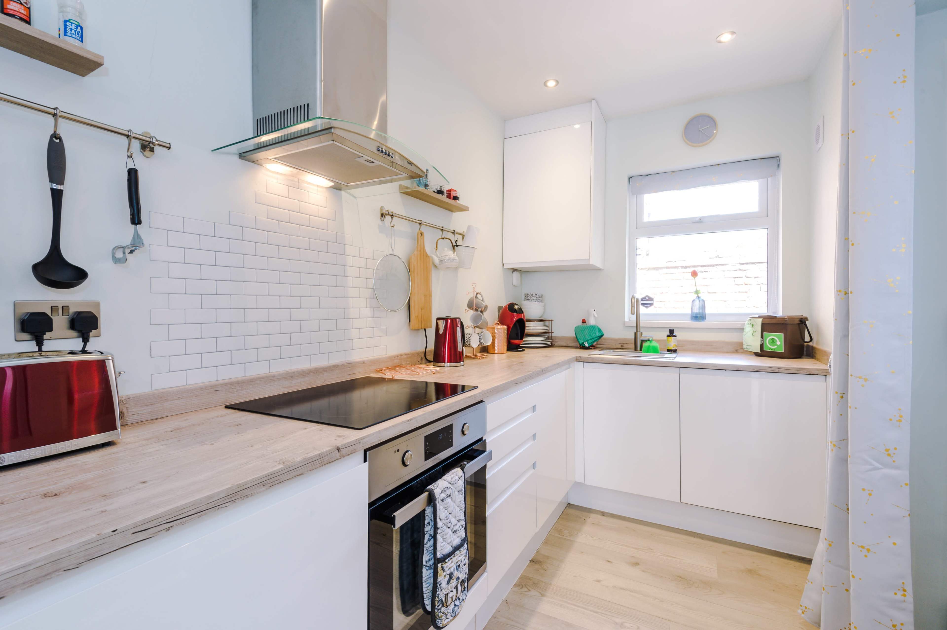 A modern kitchen with white cabinetry, a stainless steel range hood, and a wooden countertop, featuring appliances like a toaster and a kettle.