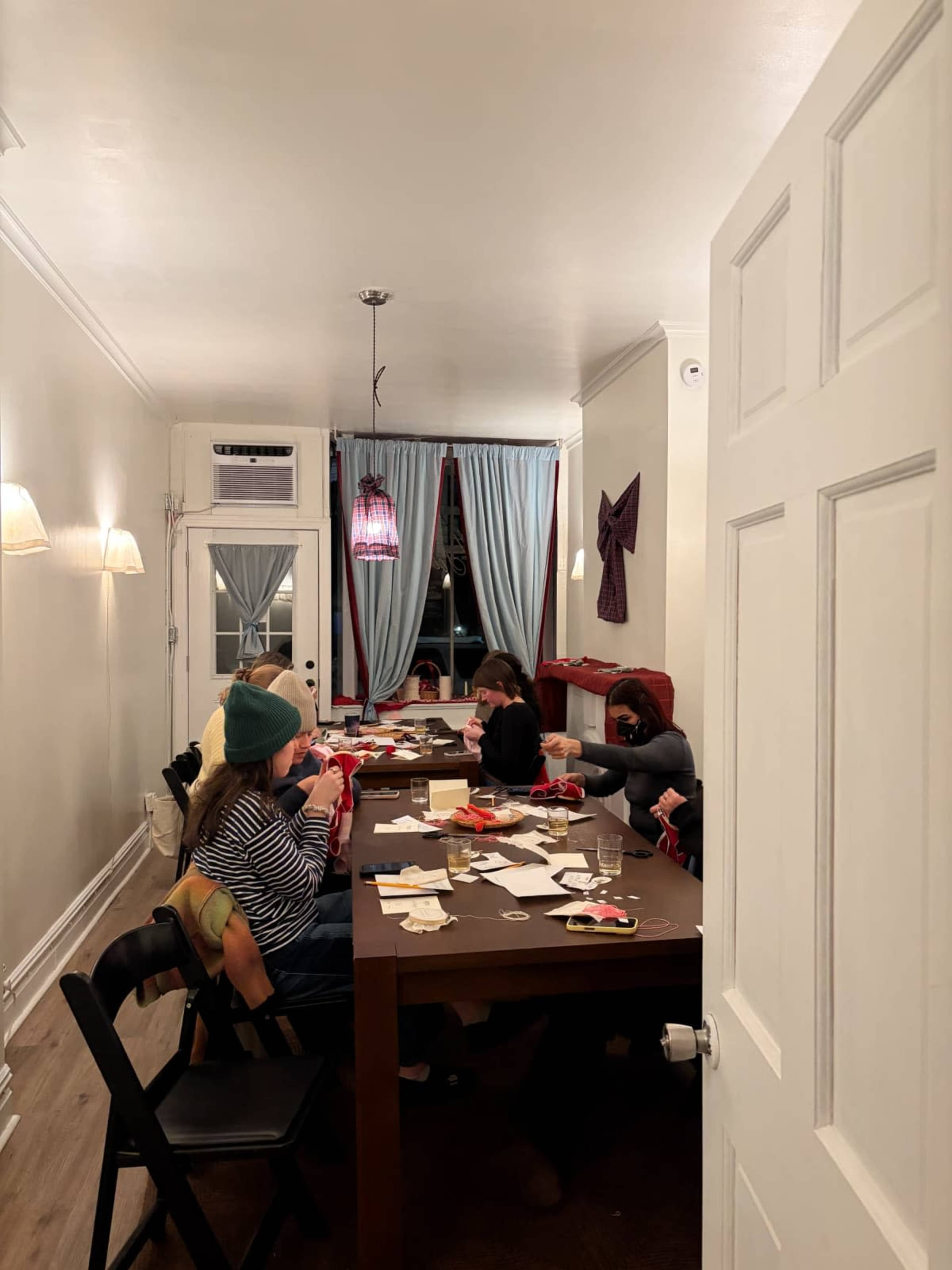 A group of people is seated around a large table engaged in a craft activity in a well-lit room with decorative curtains.