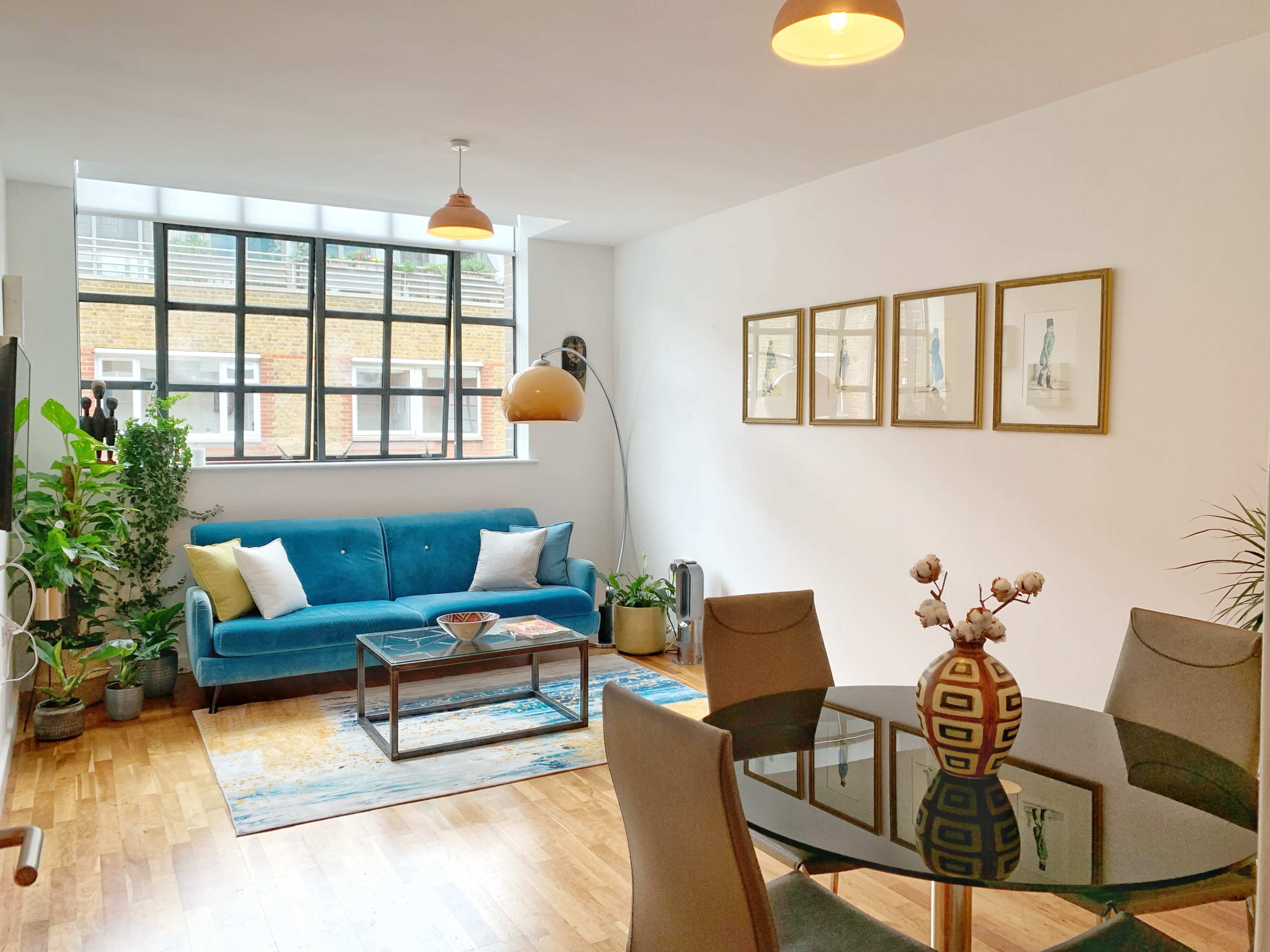 A modern living area with a blue sofa, a round dining table, and large windows letting in natural light.