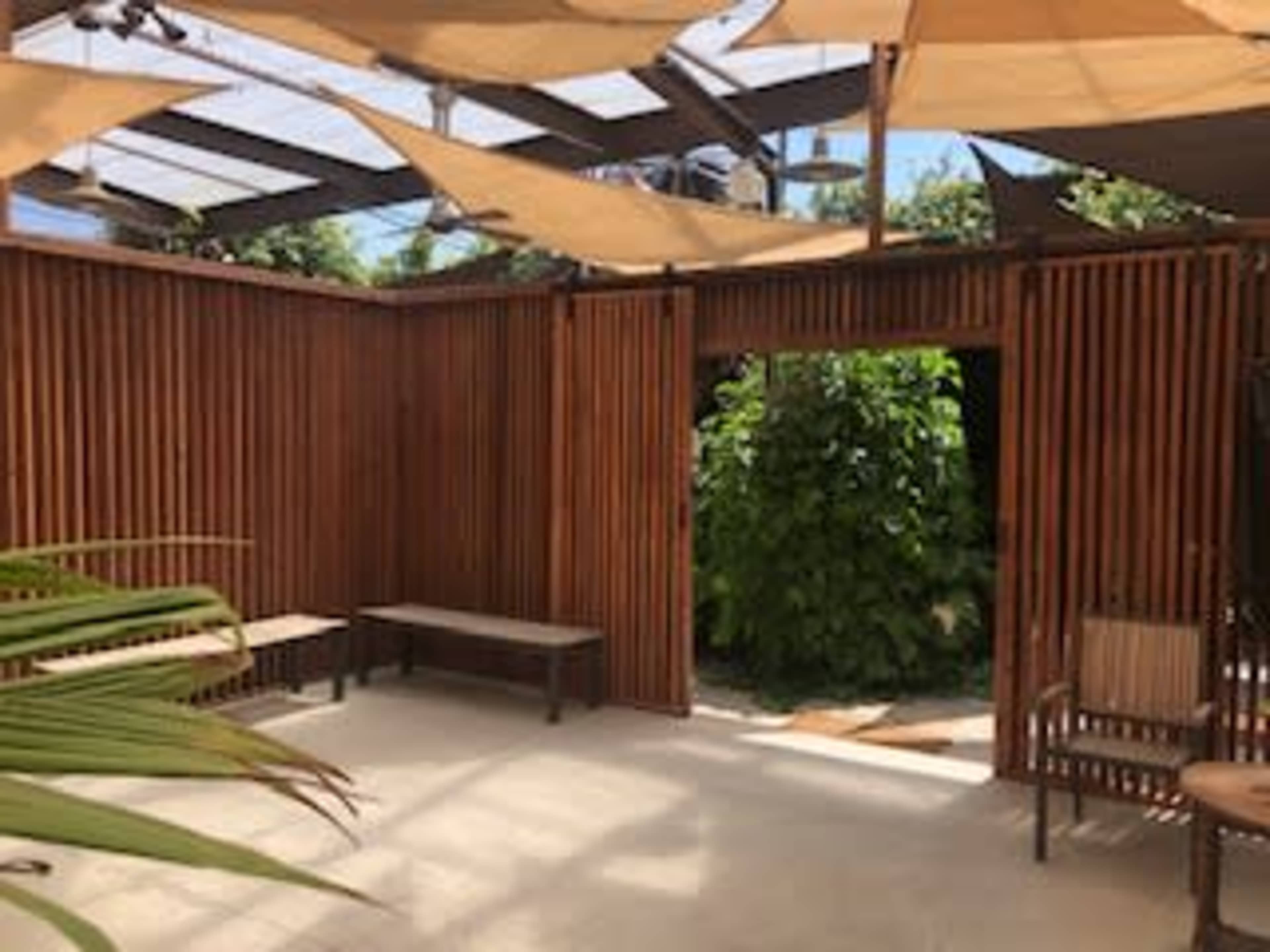 The image shows a wooden patio area with benches and a view of greenery through a slatted partition.