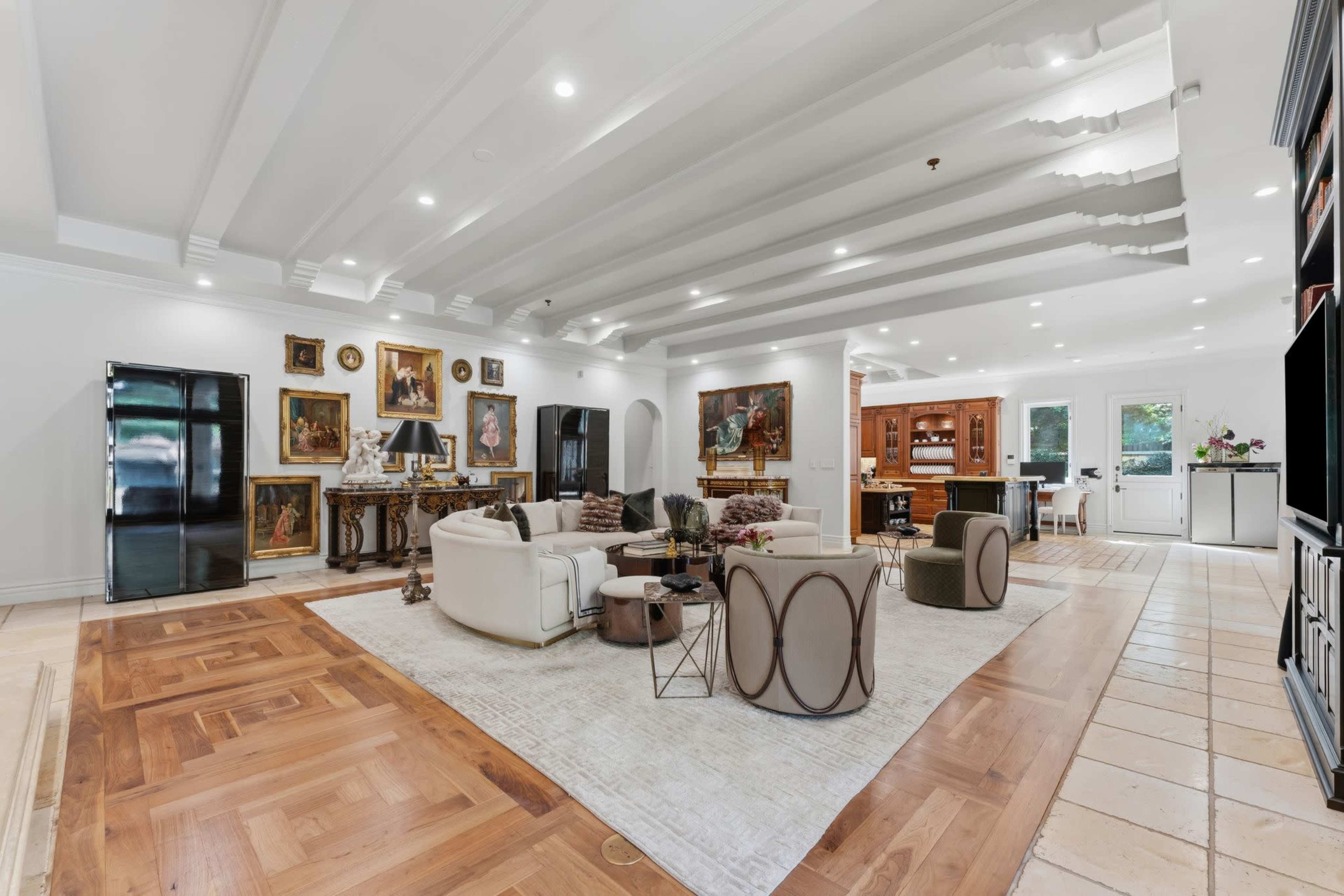 The image shows a spacious living area featuring a mix of modern furniture, a large rug, and various framed artworks on the walls.