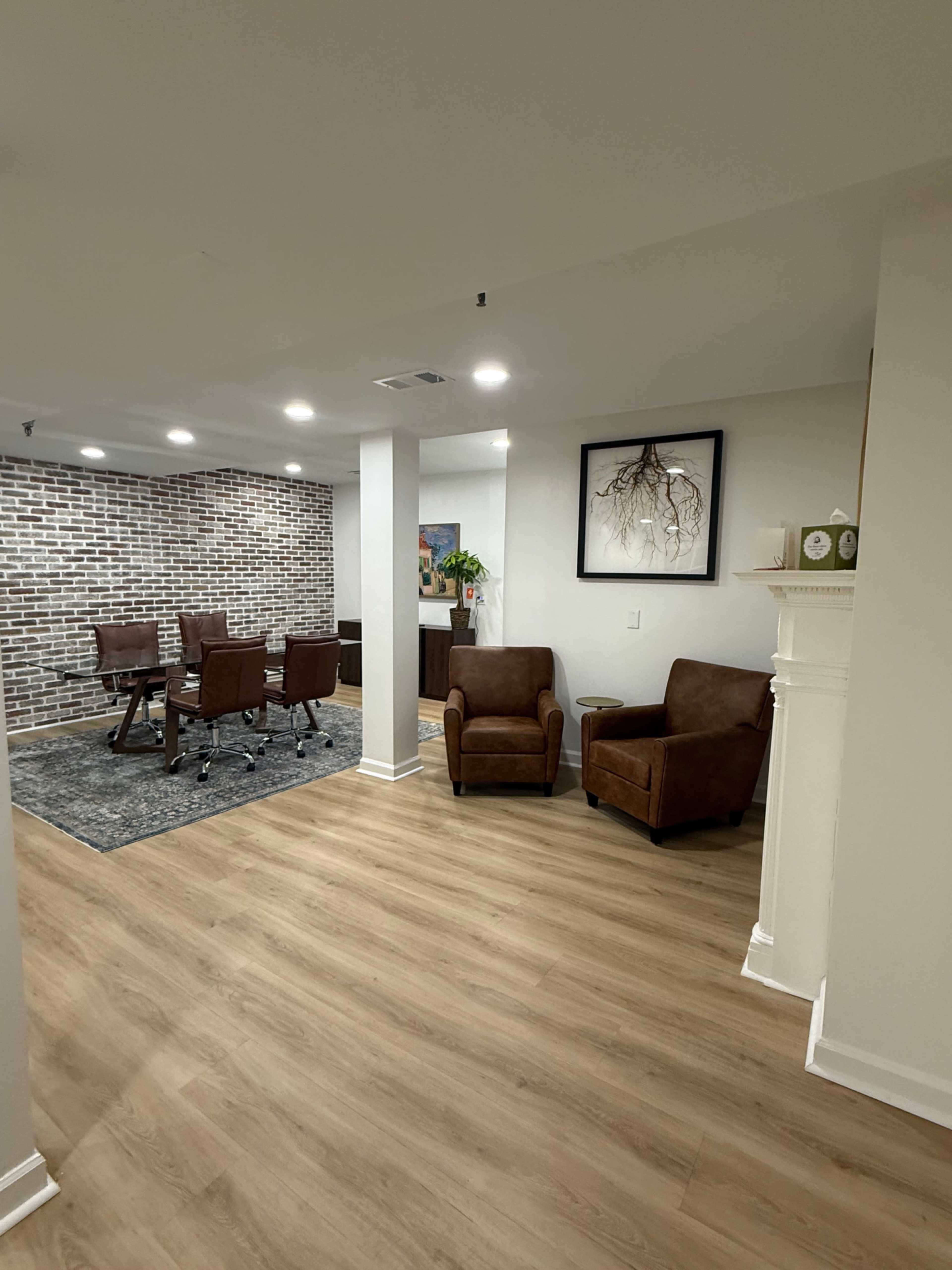 The image shows a meeting room with a brick wall, a large table surrounded by chairs, and two brown armchairs in a well-lit area.