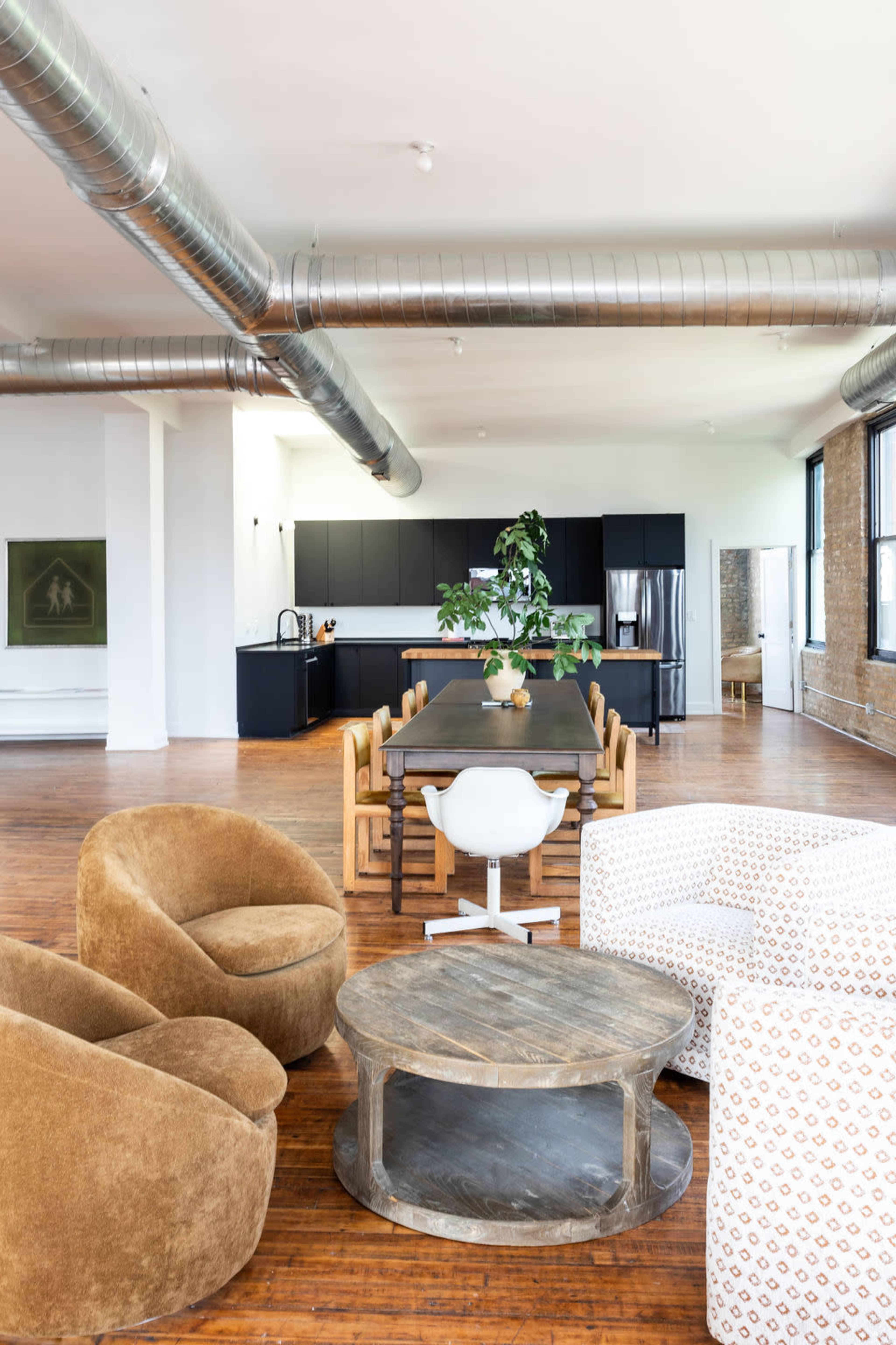 A spacious open-concept room features a large dining table, modern kitchen, and seating area with two armchairs and a coffee table.