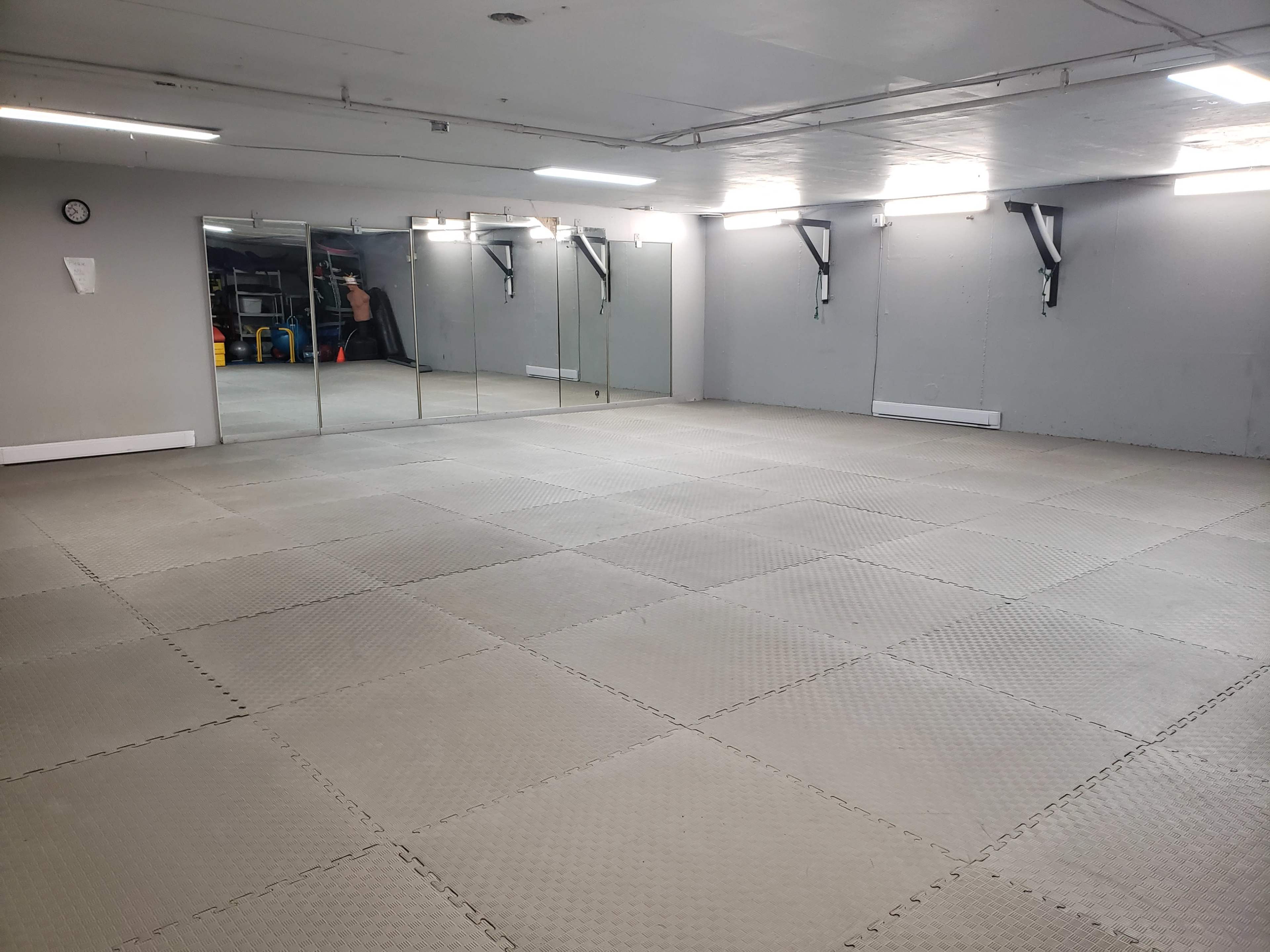 A spacious, empty room with interlocking foam tiles, large mirrors on one wall, and minimal furnishings.