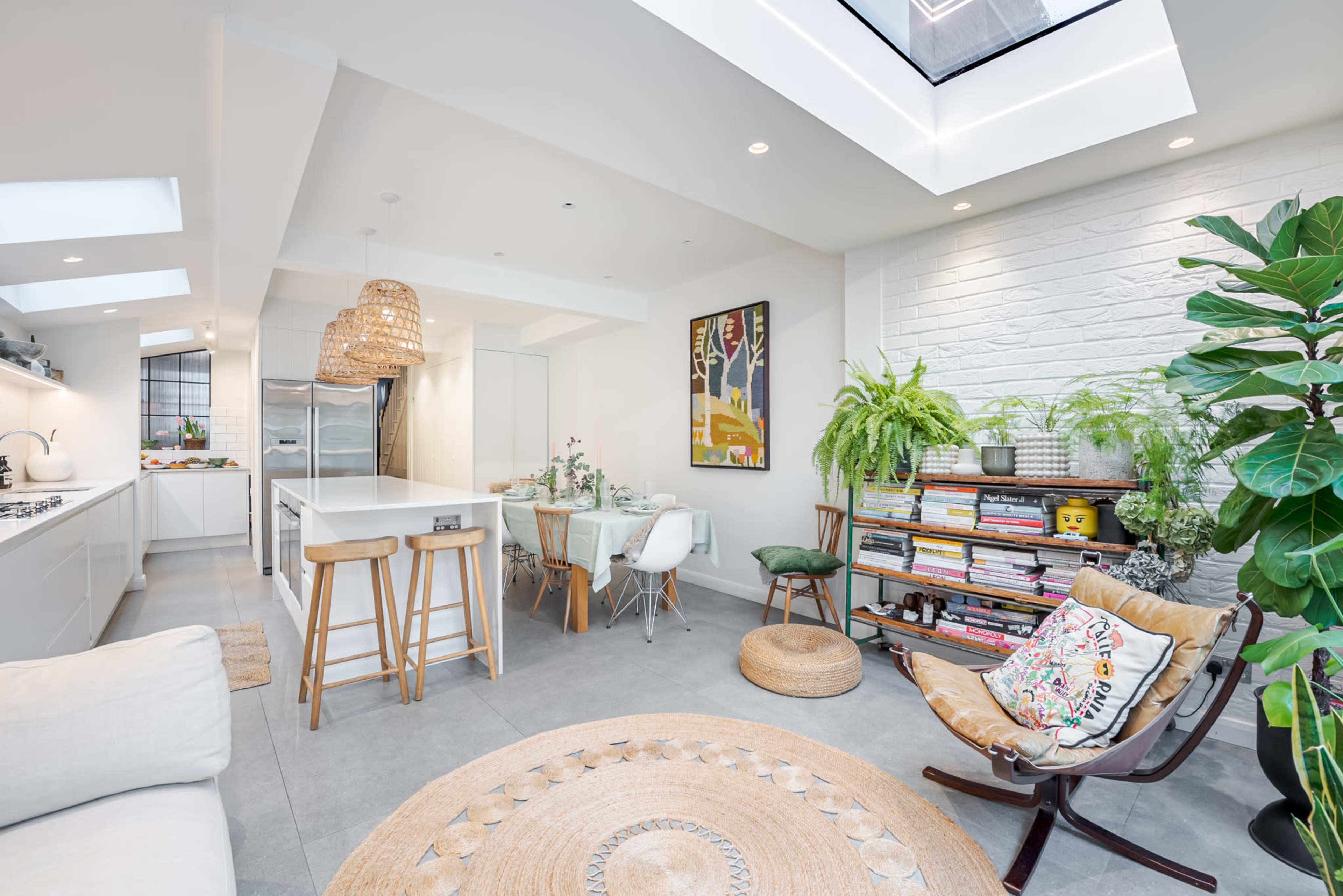 A modern kitchen and living area with a skylight, showcasing a dining table, decorative plants, and a cozy seating arrangement.