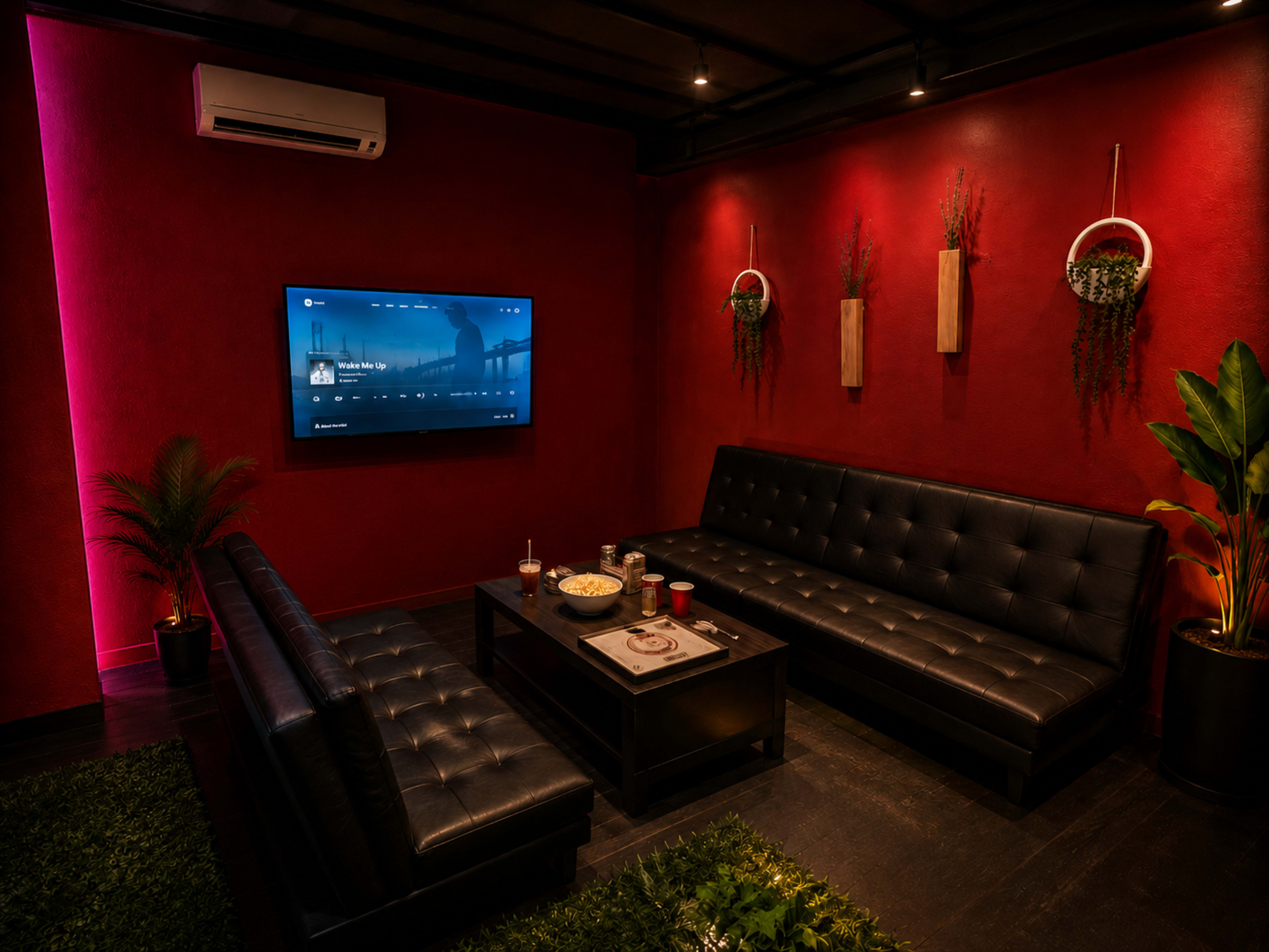 A cozy lounge area features black leather sofas, a central coffee table, and a wall-mounted TV, all set against a deep red backdrop with modern decor.