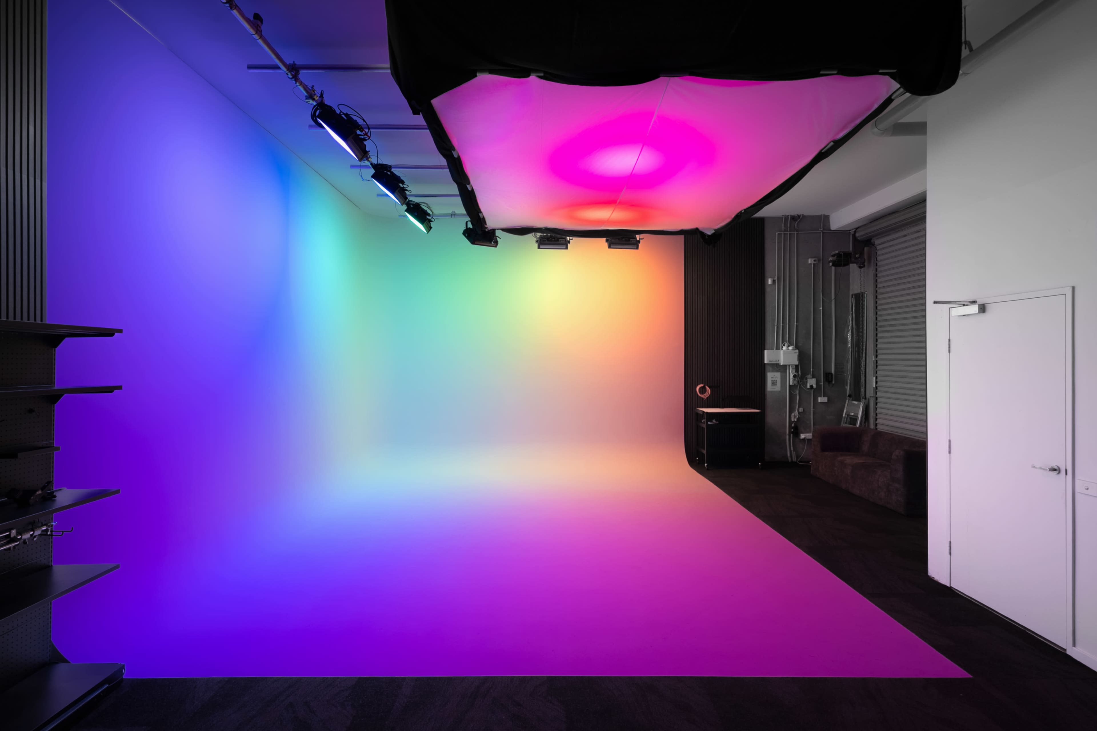 The image shows a studio space with a gradient backdrop featuring vibrant colors, in a modern setting with minimal furnishings.