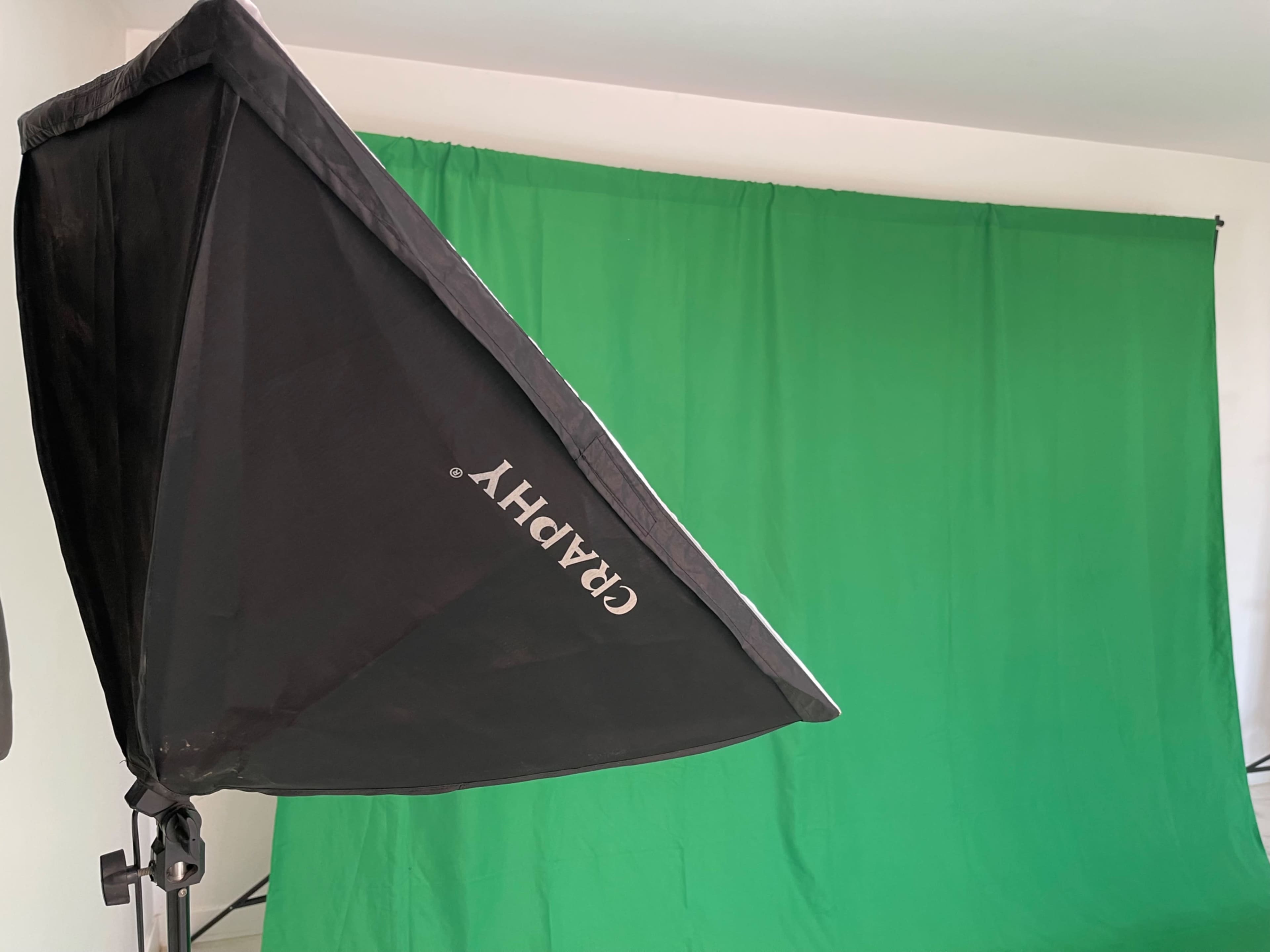 A black light umbrella positioned to the side of a green backdrop in an indoor setting.