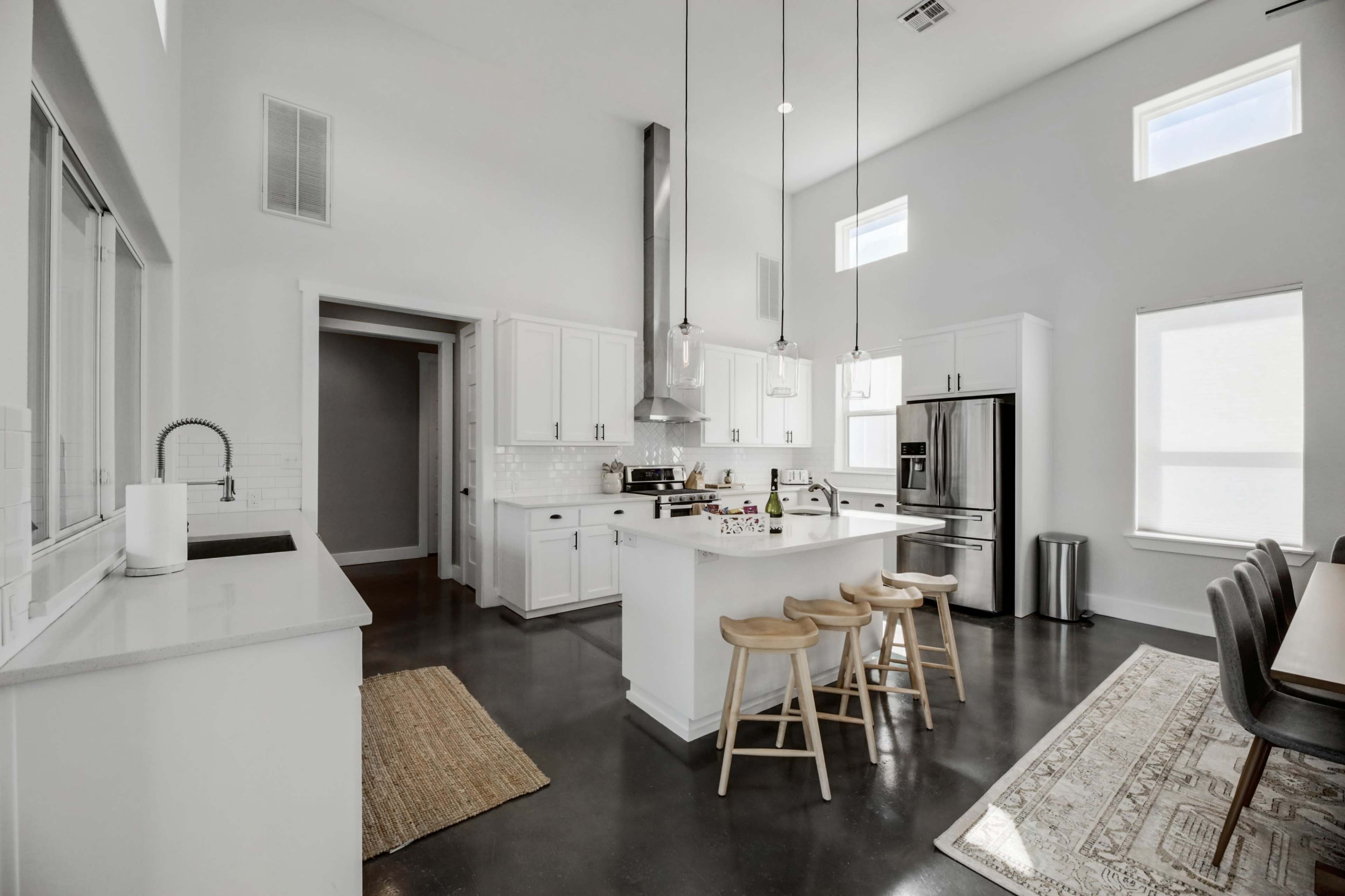 A modern kitchen featuring white cabinetry, stainless steel appliances, and a central island with three wooden stools.