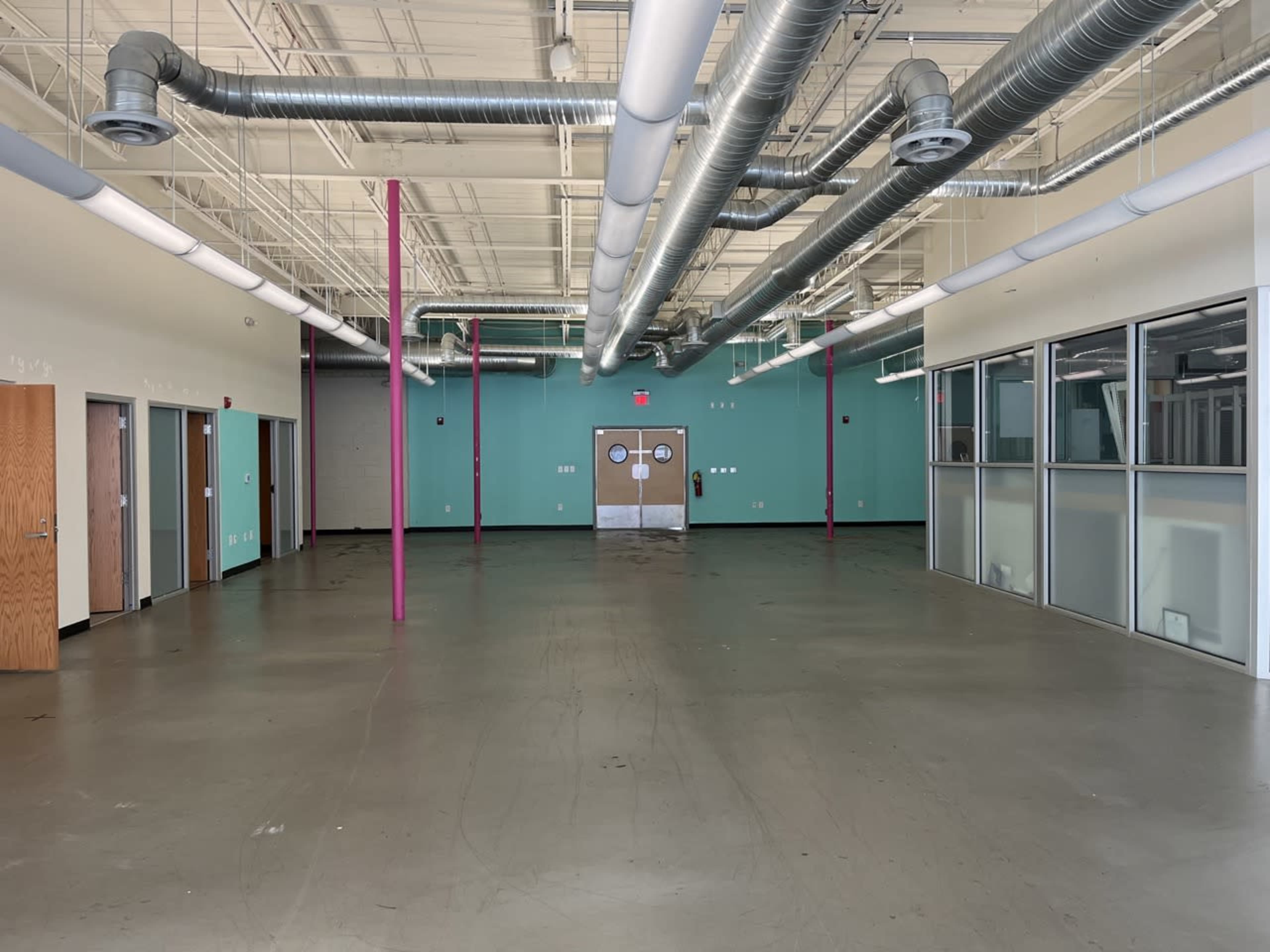 An empty commercial space with concrete flooring, large windows, and exposed ductwork on the ceiling.