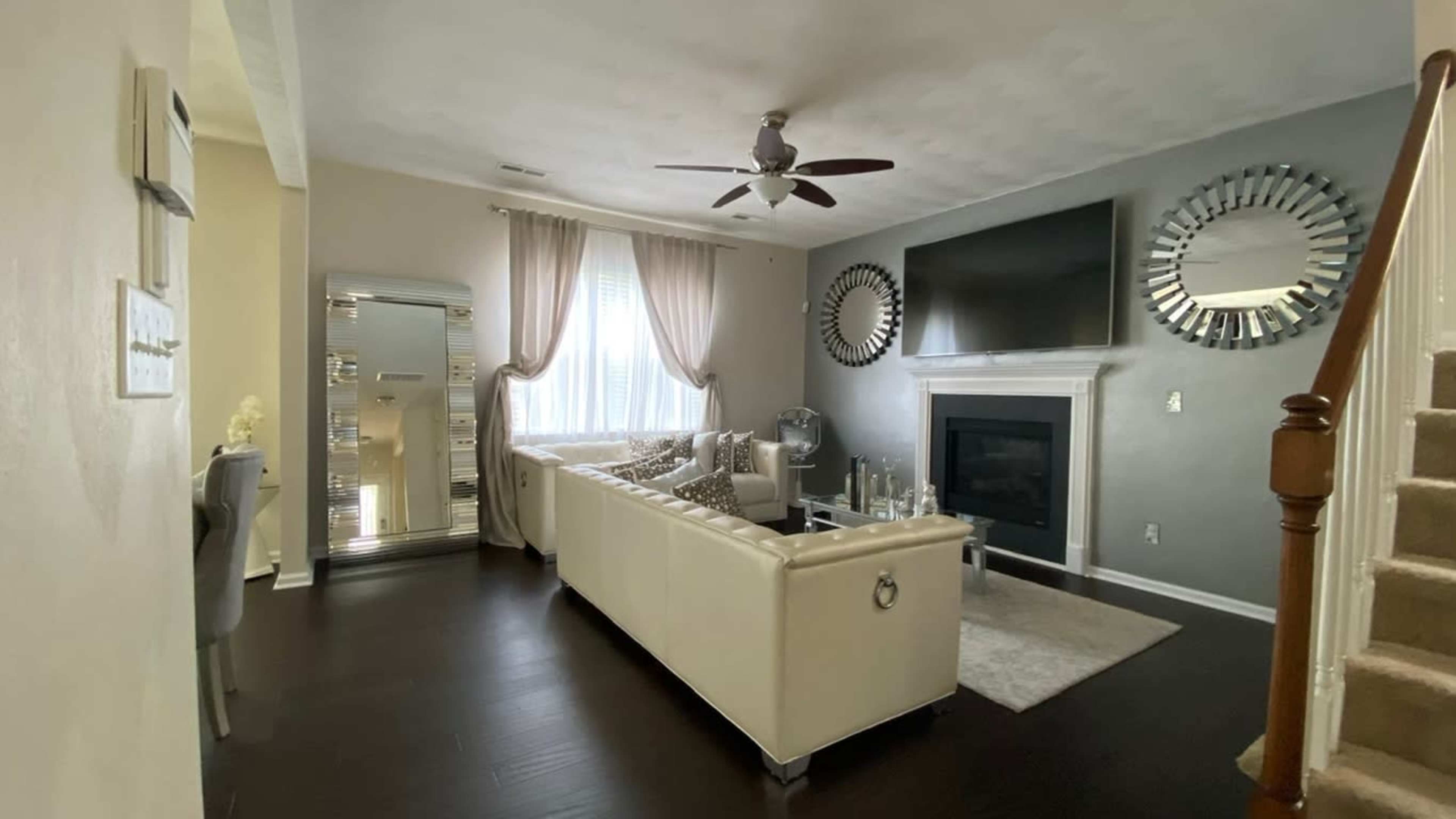 A modern living room with a white sectional sofa, a large television mounted above a fireplace, and mirrors on the walls.