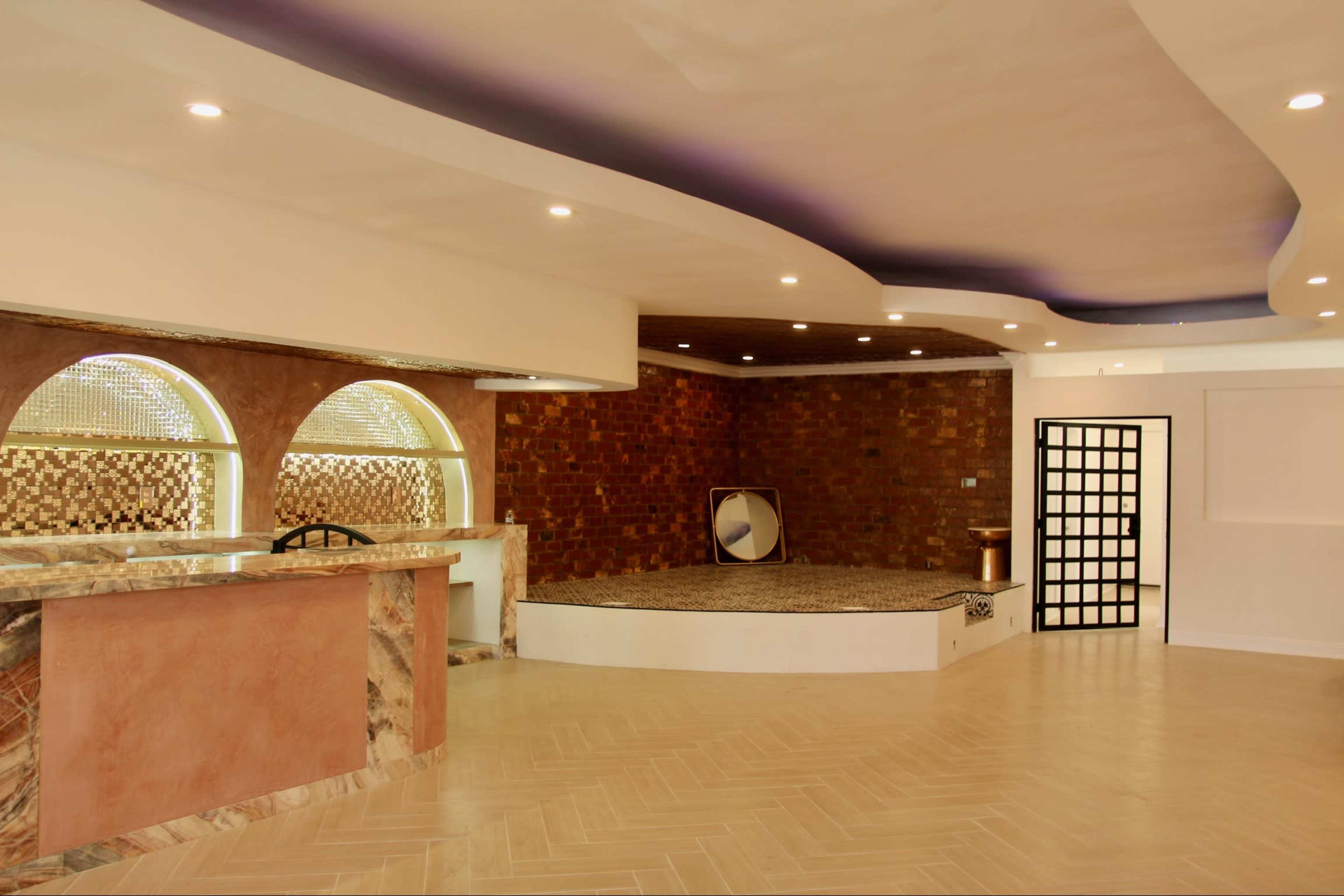 The image shows a spacious interior room with a polished floor, a bar counter, and a raised seating area with brick wall accents.