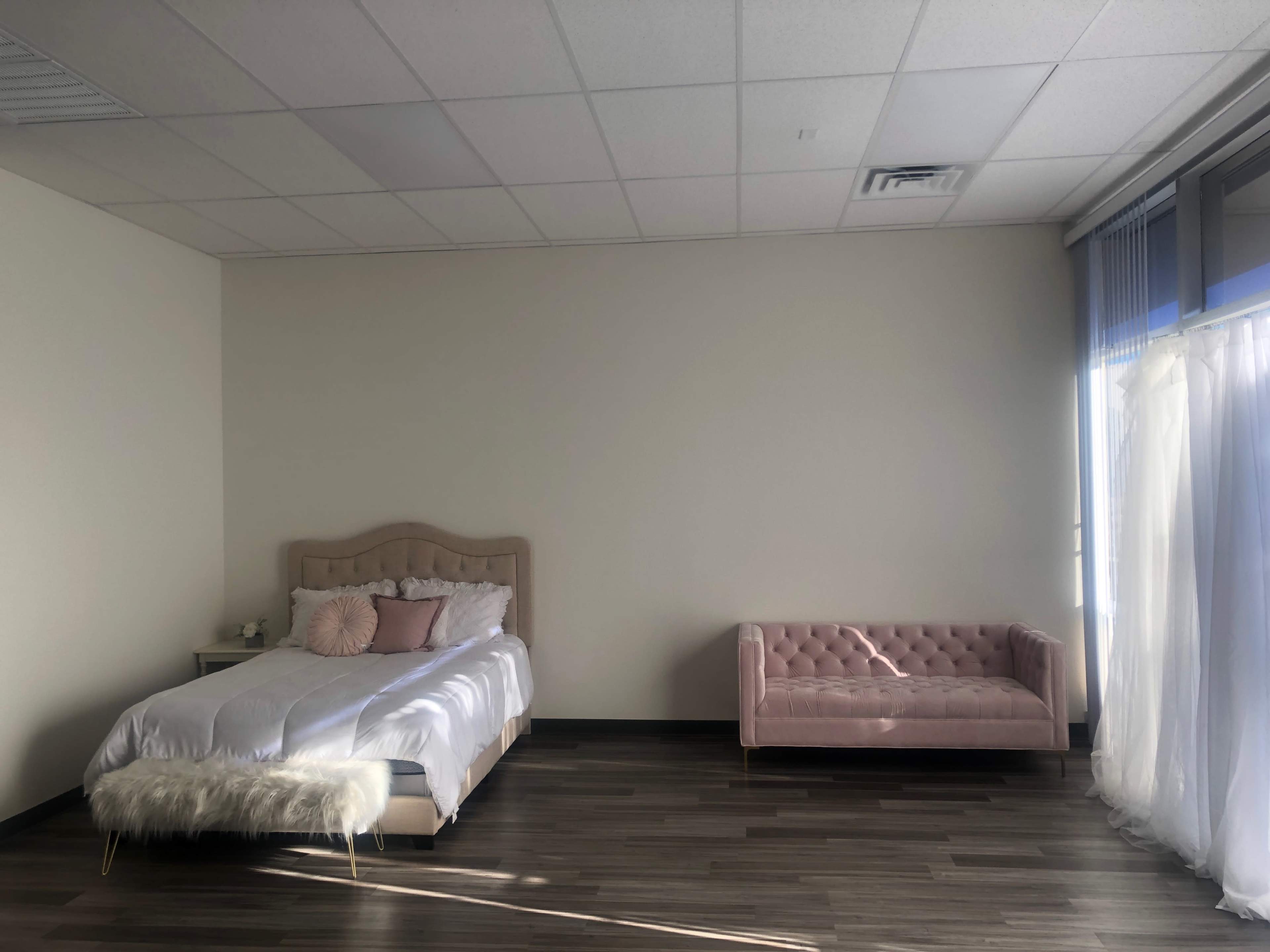 A minimalist bedroom with a neatly made bed and a pink upholstered sofa against a light-colored wall.