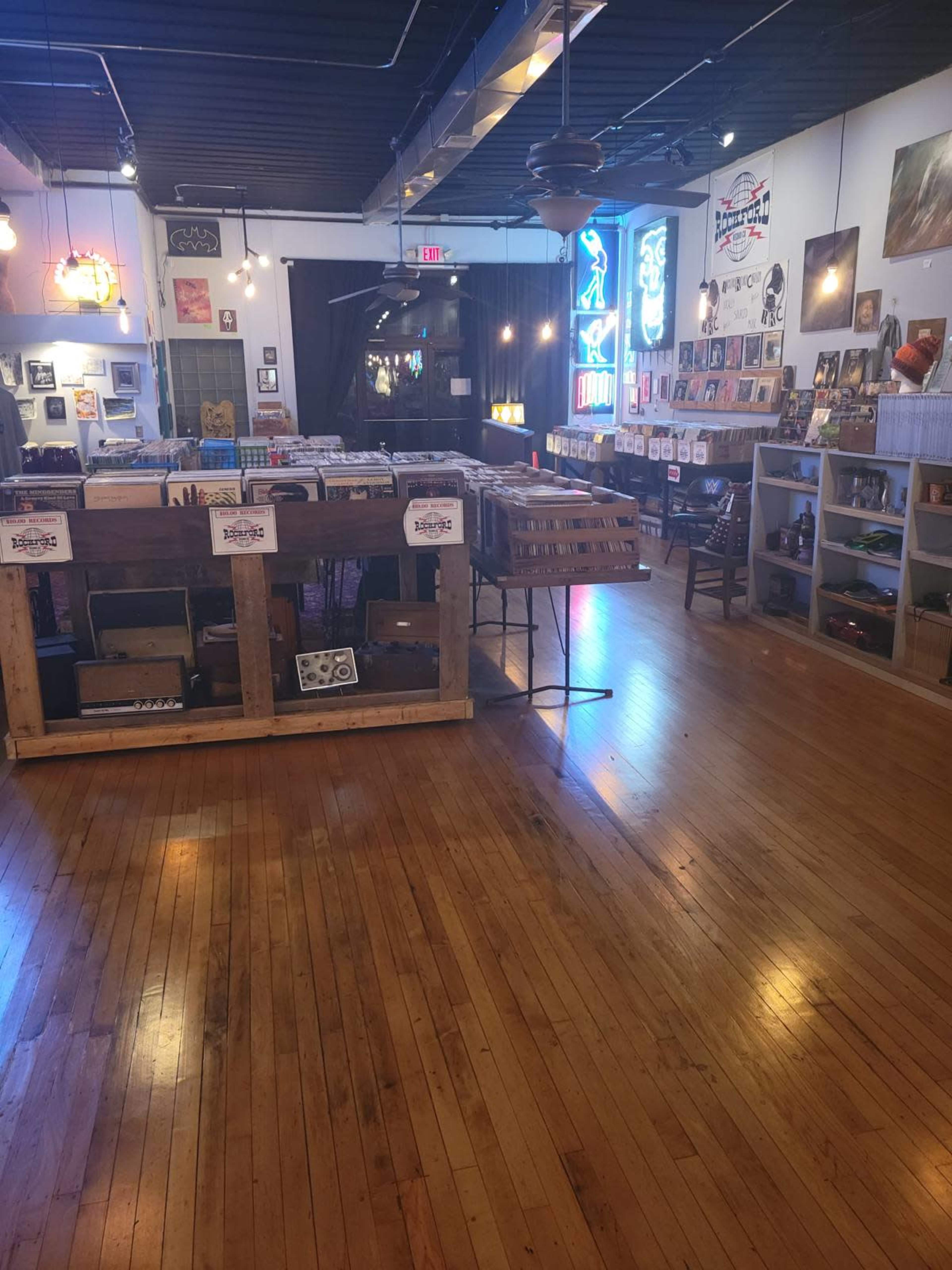 The interior of a vinyl record store features wooden flooring and displays of records organized on shelves and tables.