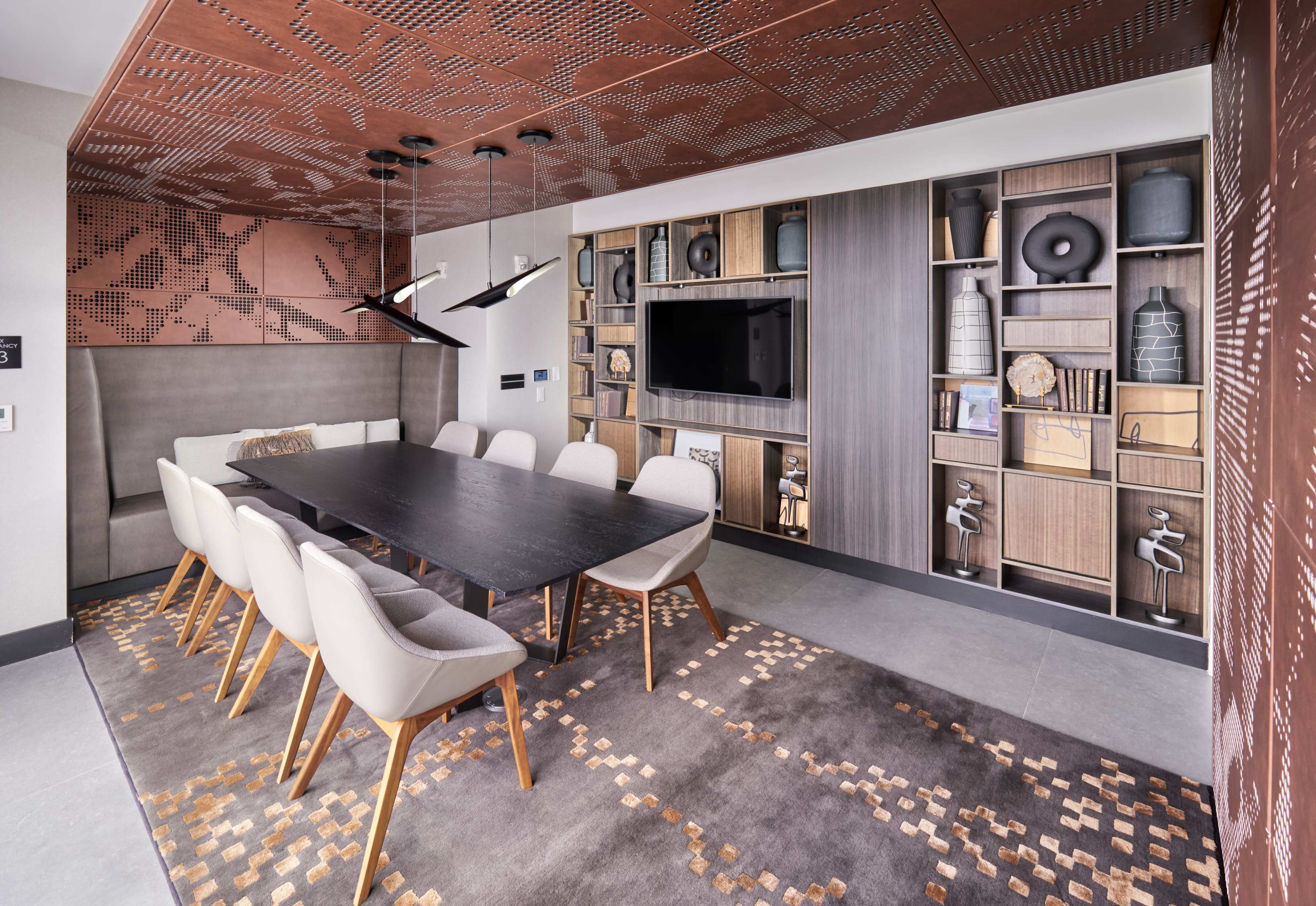 A modern conference room features a long black table surrounded by white chairs, with a backdrop of stylish wall décor and a built-in media unit.