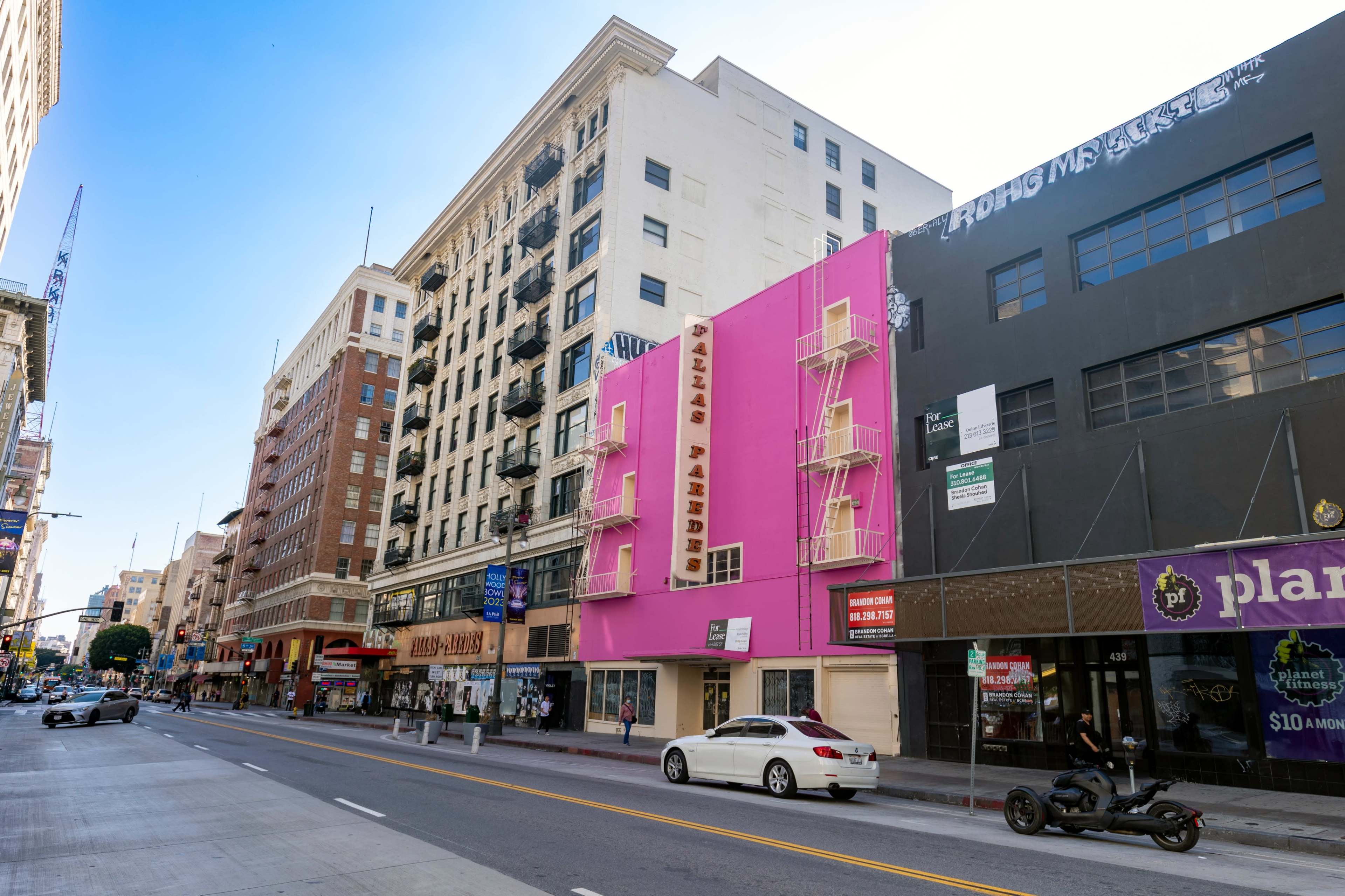 The image shows a street scene featuring a tall, colorful pink building labeled "Palace" alongside other commercial buildings in an urban area.