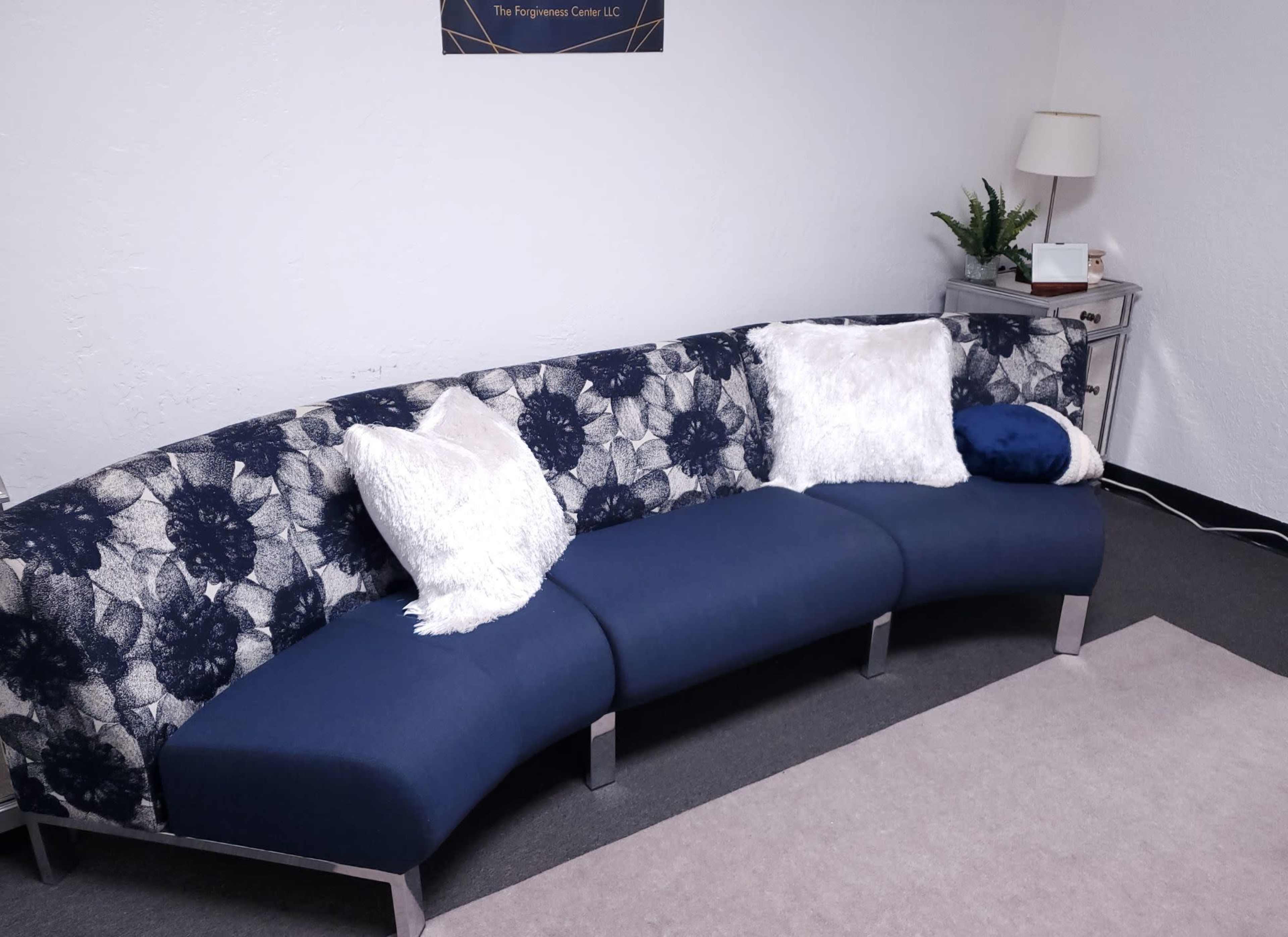 A curved navy blue sofa with decorative pillows sits against a white wall in a room with a small side table and a plant.