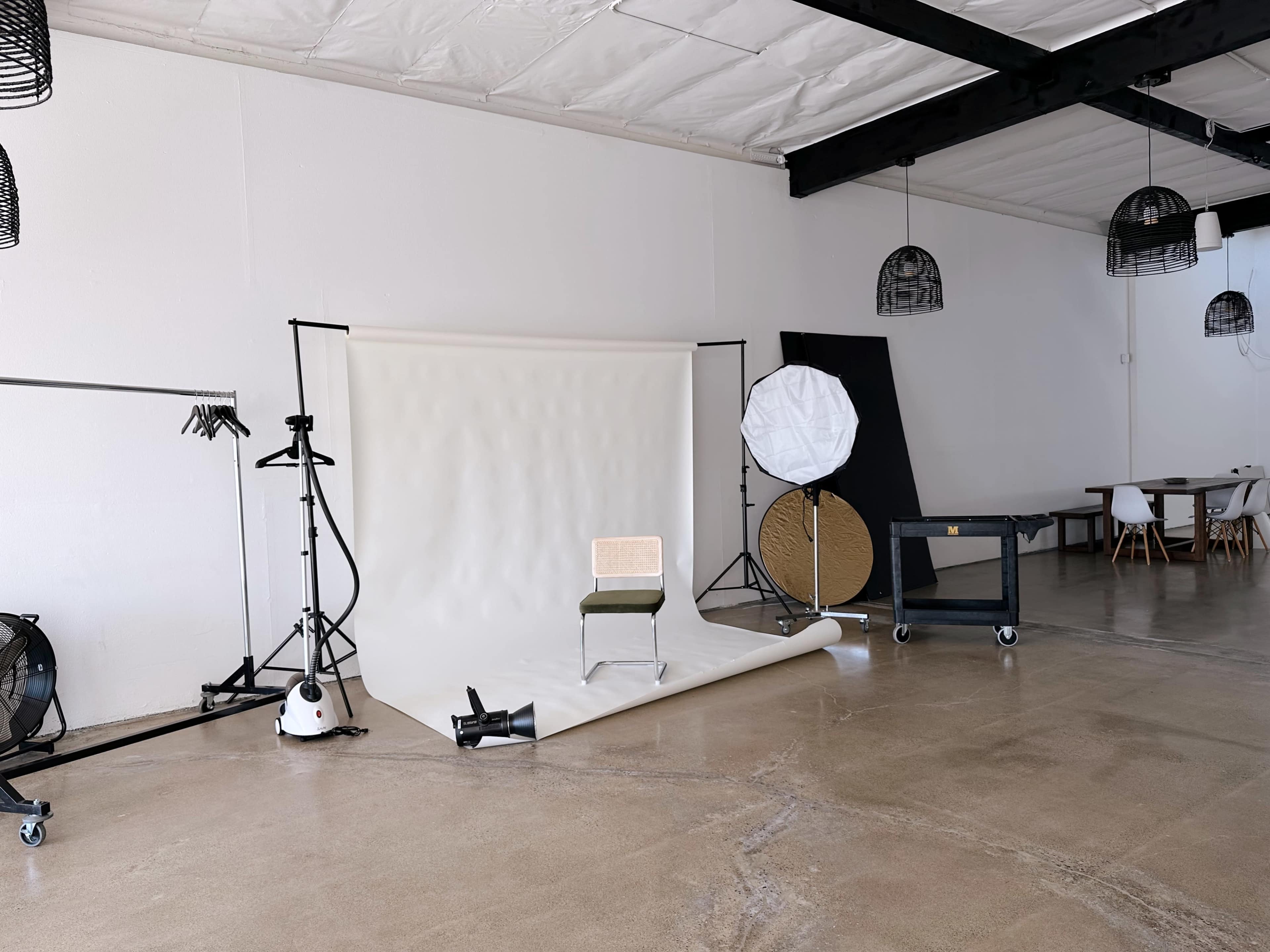 A minimalist studio space features a light backdrop with a chair, photography equipment, and a cart in an open area with polished concrete floors.