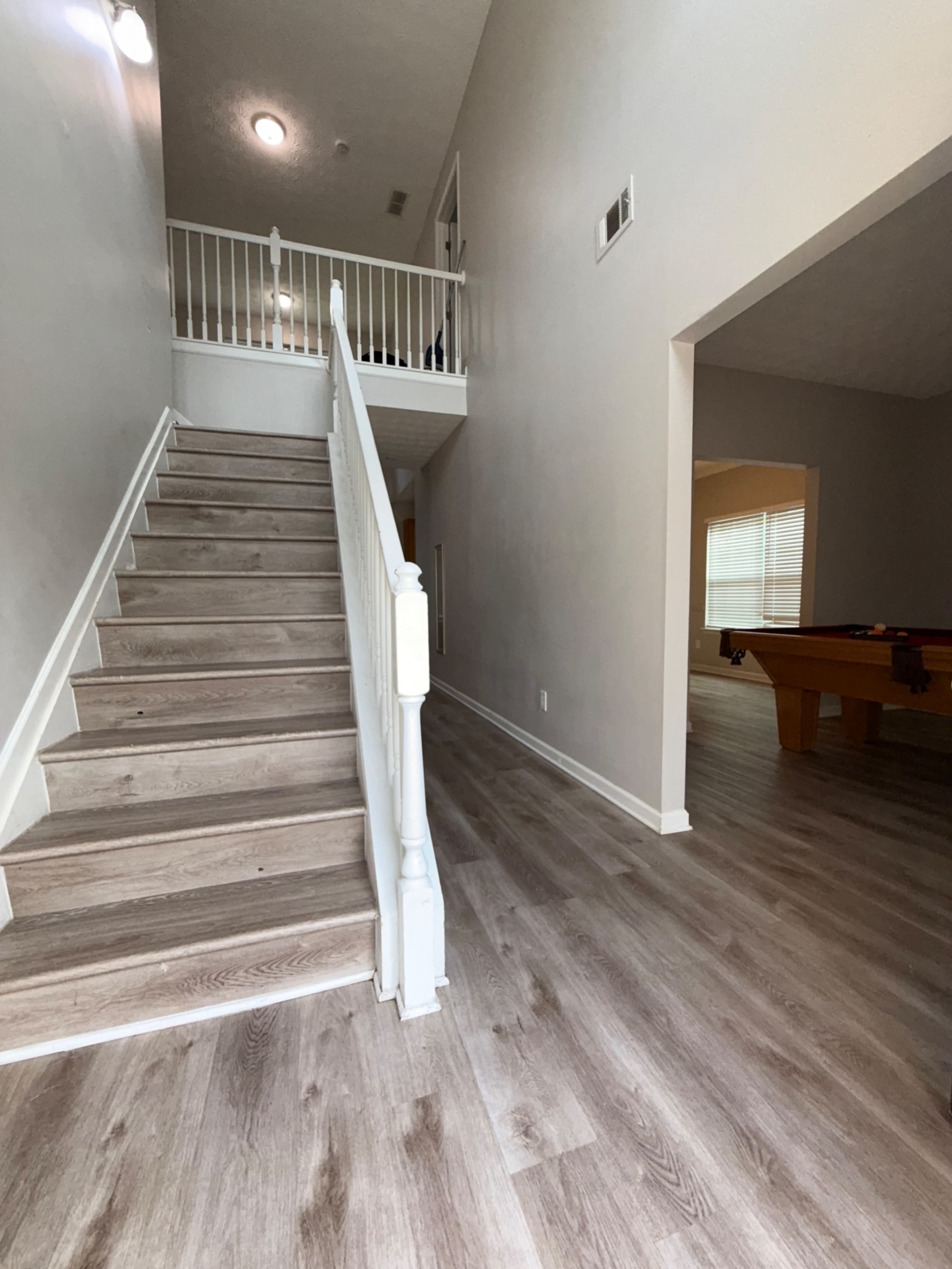 A downward view of a light-colored stairwell leading to an open hallway, with a pool table visible in a separate room.