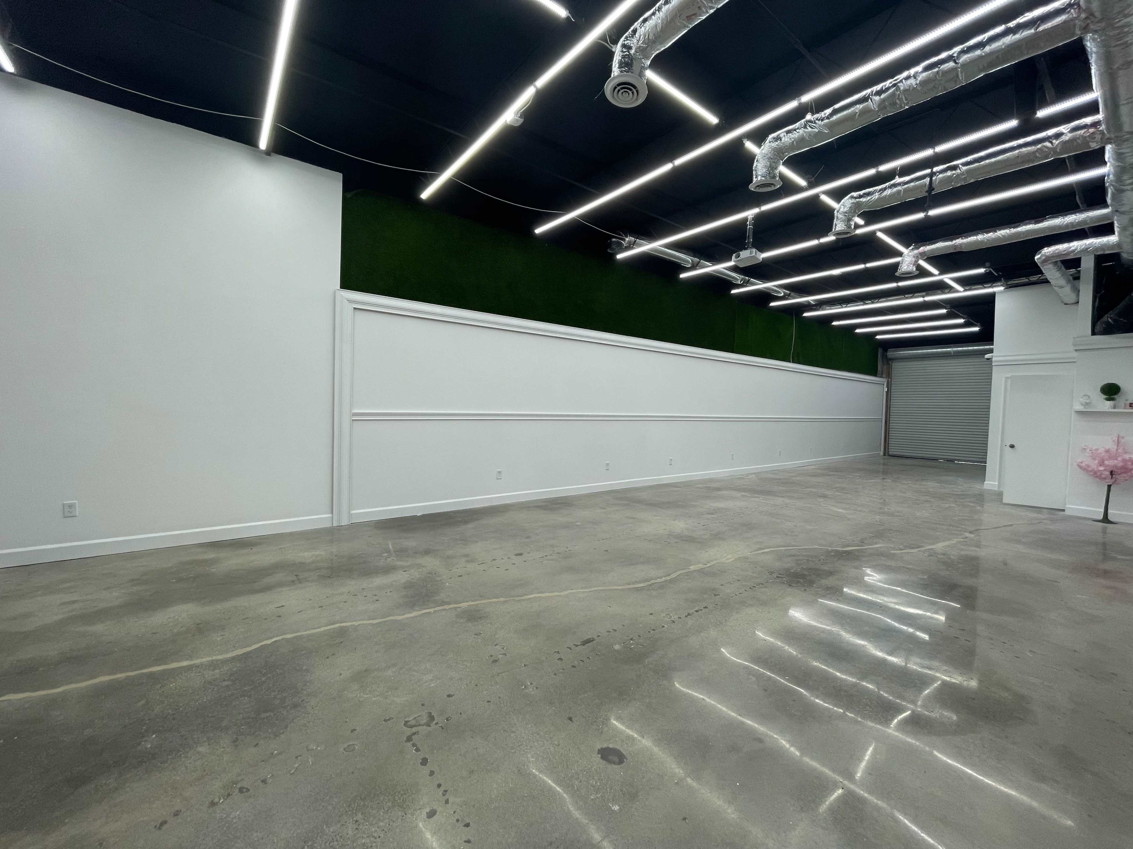 An empty commercial space with polished concrete floors, bright overhead lighting, and a green accent wall.