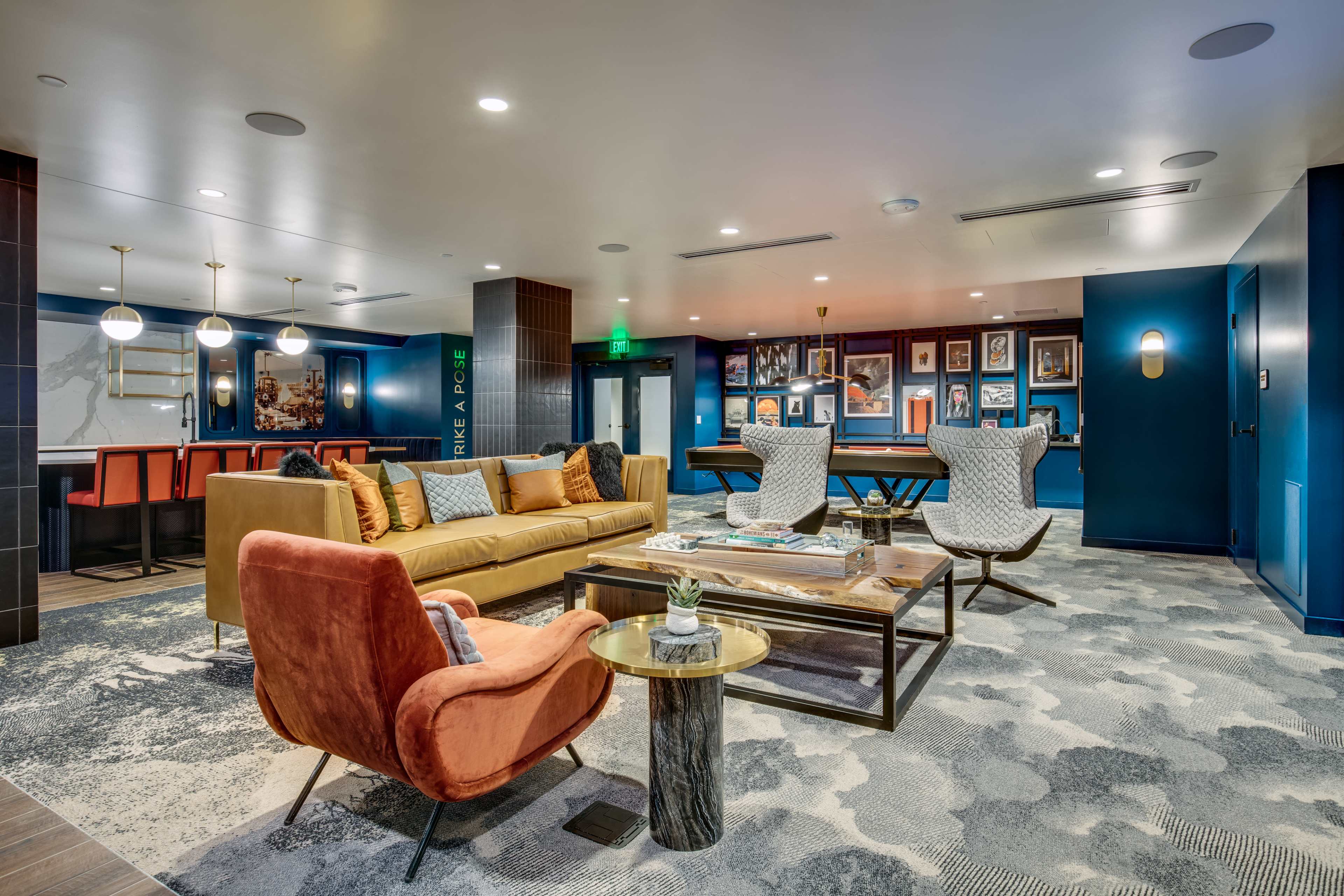 A modern lounge area featuring comfortable seating, a coffee table, and wall-mounted artwork, with a bar area visible in the background.