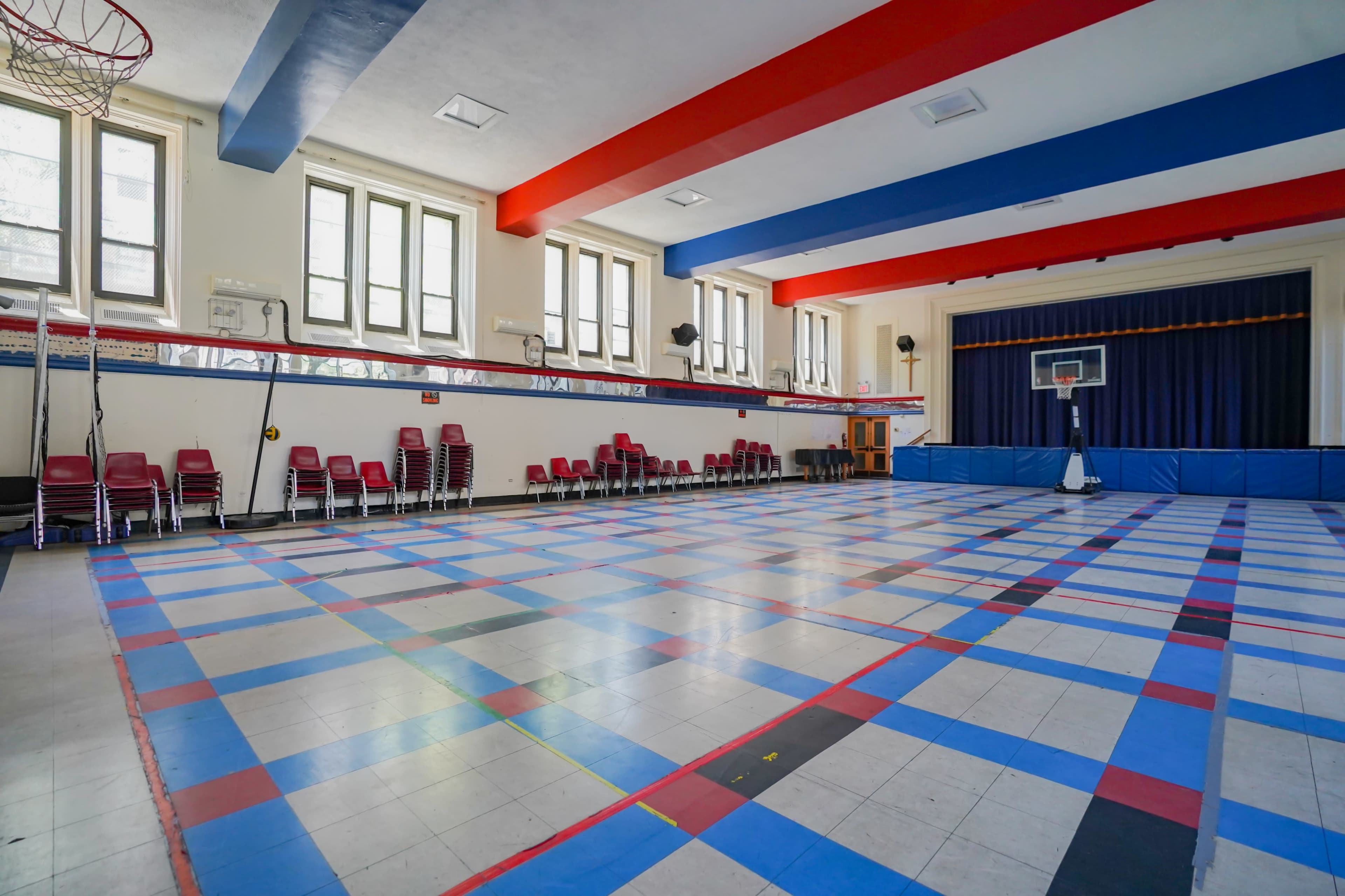 A brightly colored empty gymnasium with a basketball hoop and tiled floor featuring a checkerboard pattern of blue, red, and white squares.