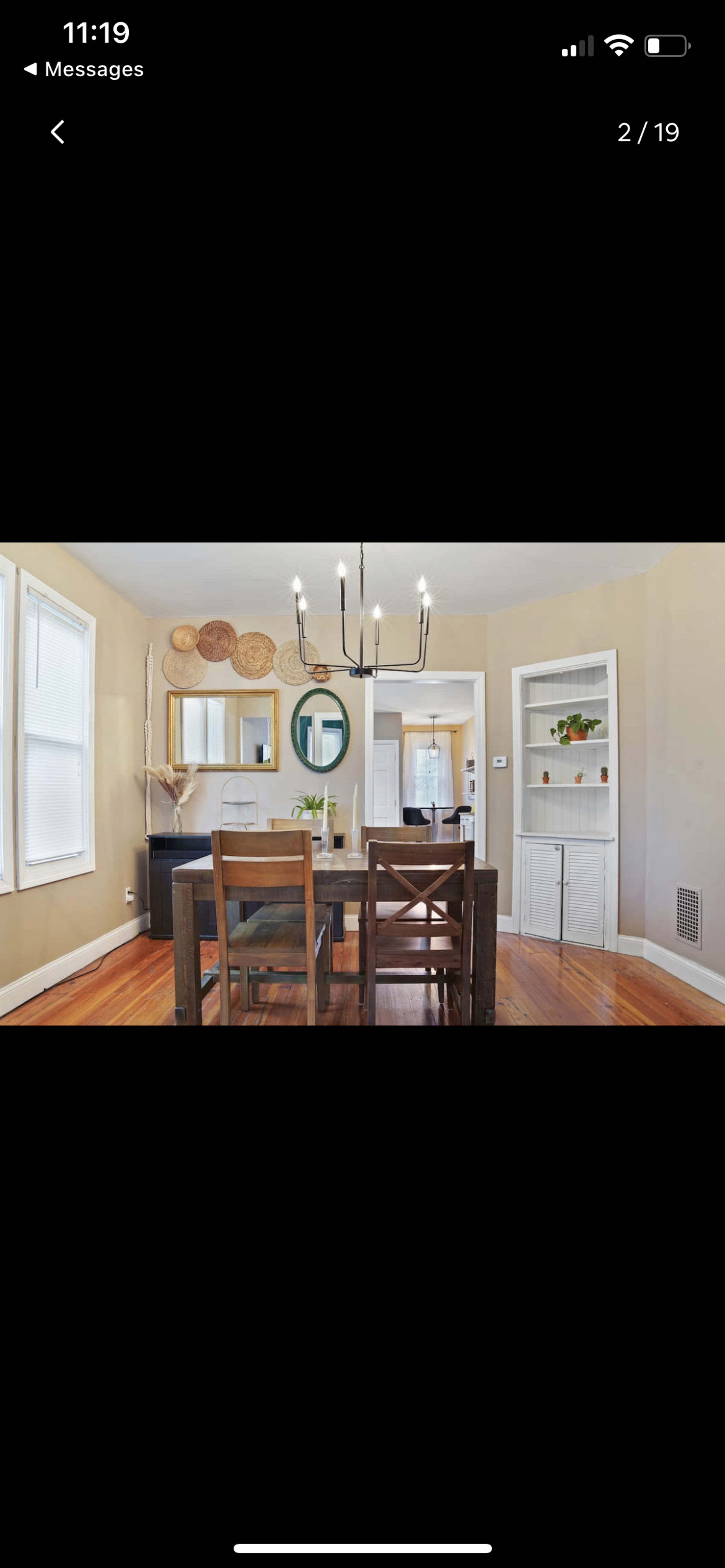 A dining area features a wooden table surrounded by chairs, with a chandelier overhead and a mirrored wall accent.