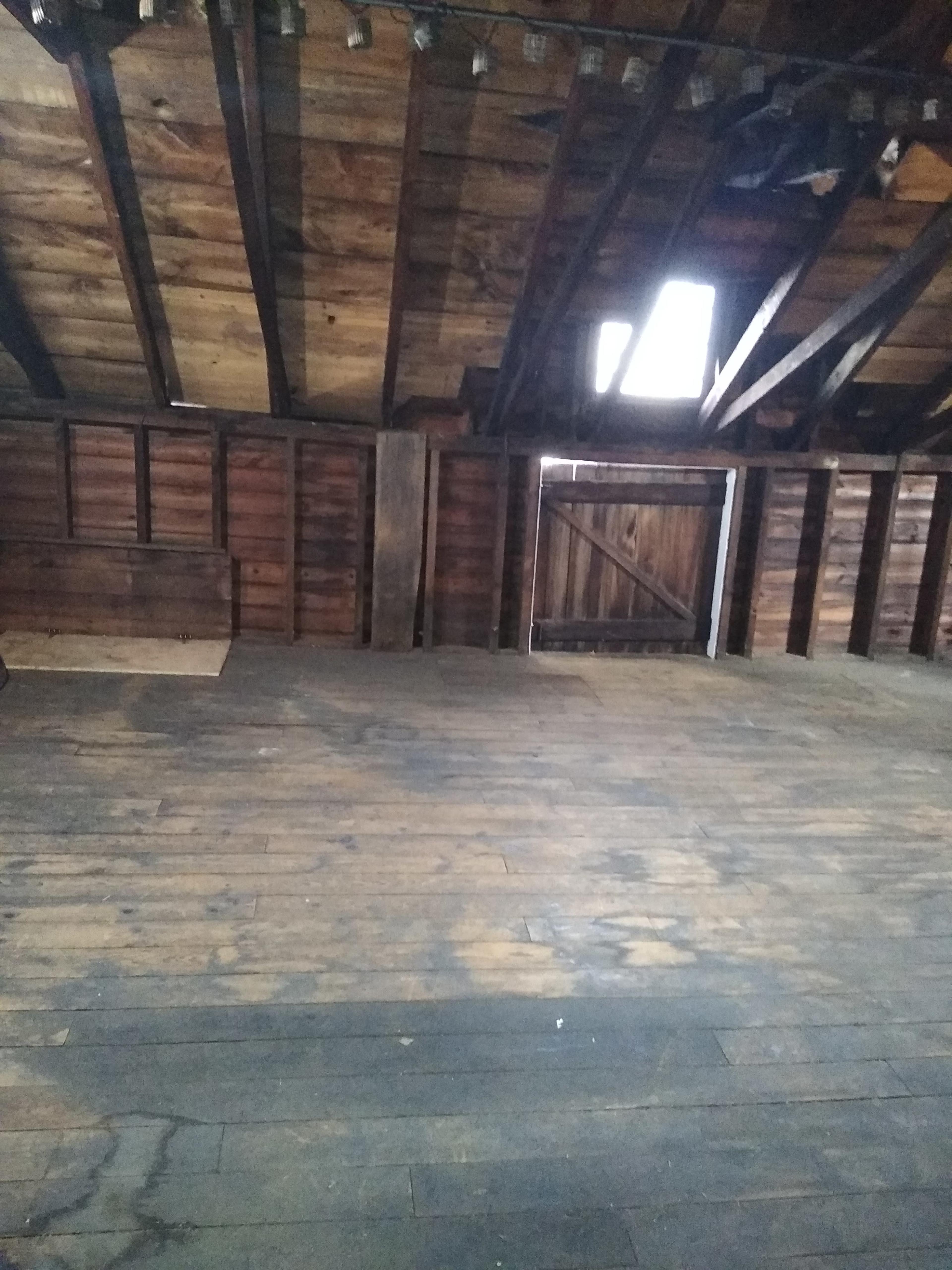 An empty attic with wooden beams and a boarded window.