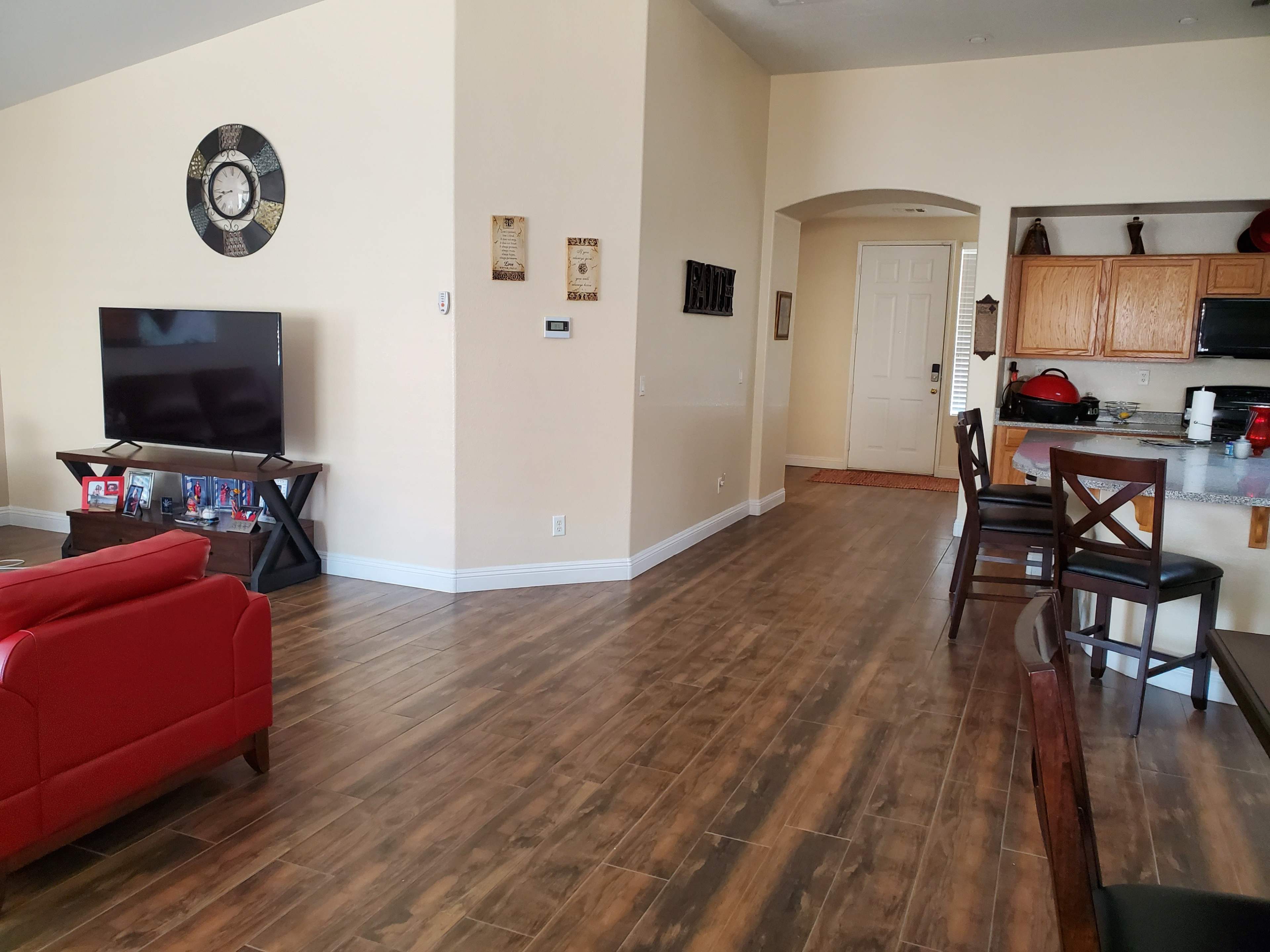 A modern living room with red seating, hardwood floors, and a view of a kitchen area through an archway.