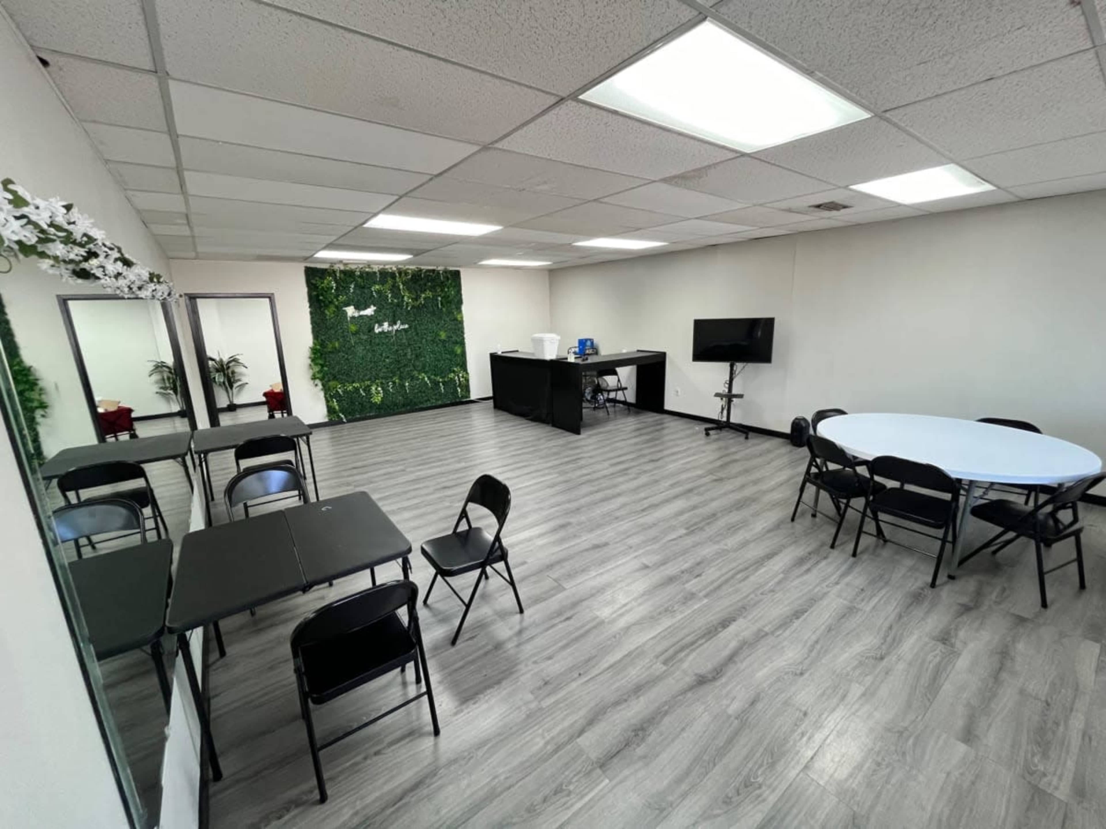 The image shows a spacious room with a green accent wall, several tables and chairs arranged for seating, and a television mounted on a wall.