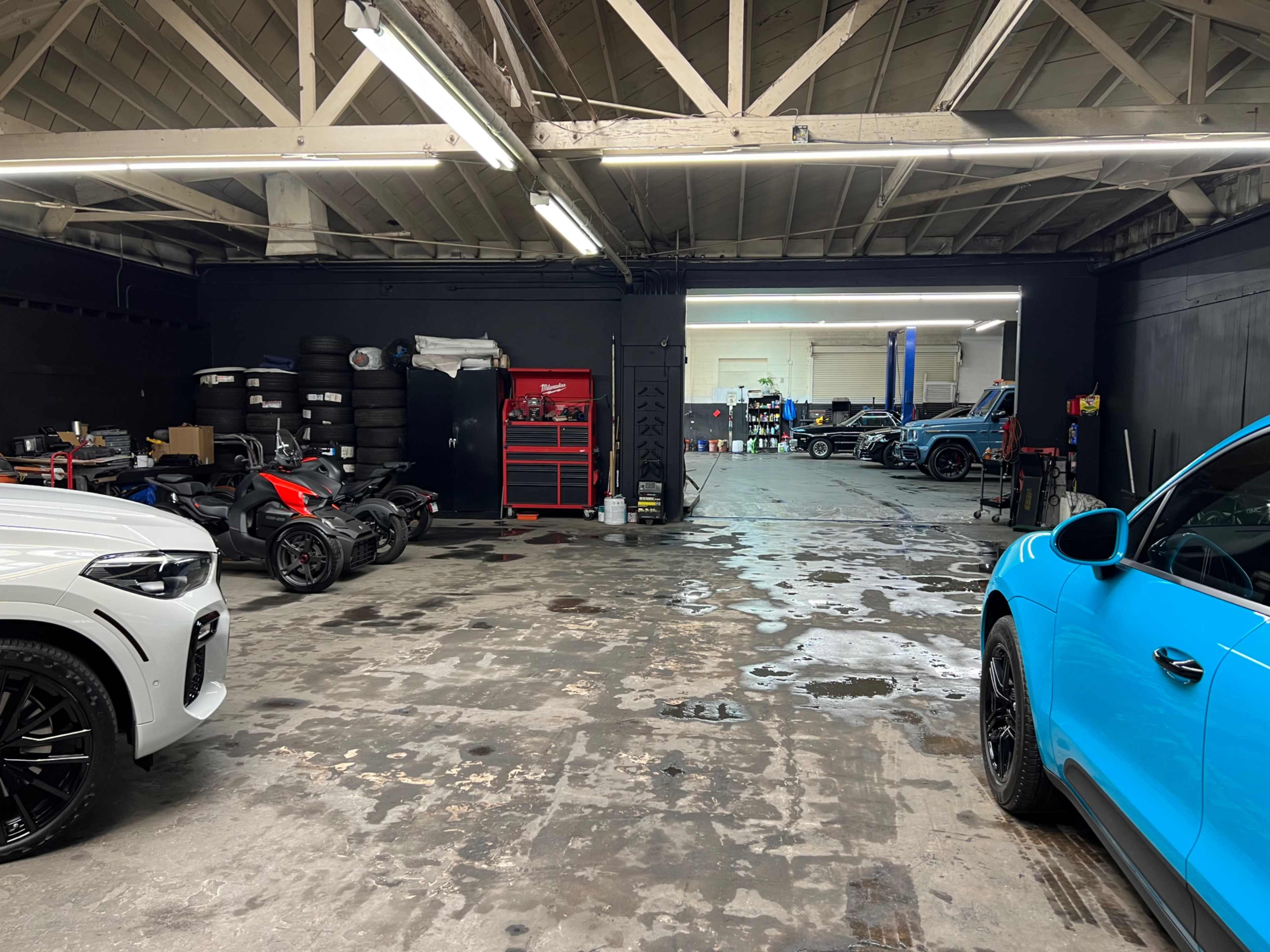A garage with several vehicles, including a white car and a blue vehicle, along with tools and equipment in the background.