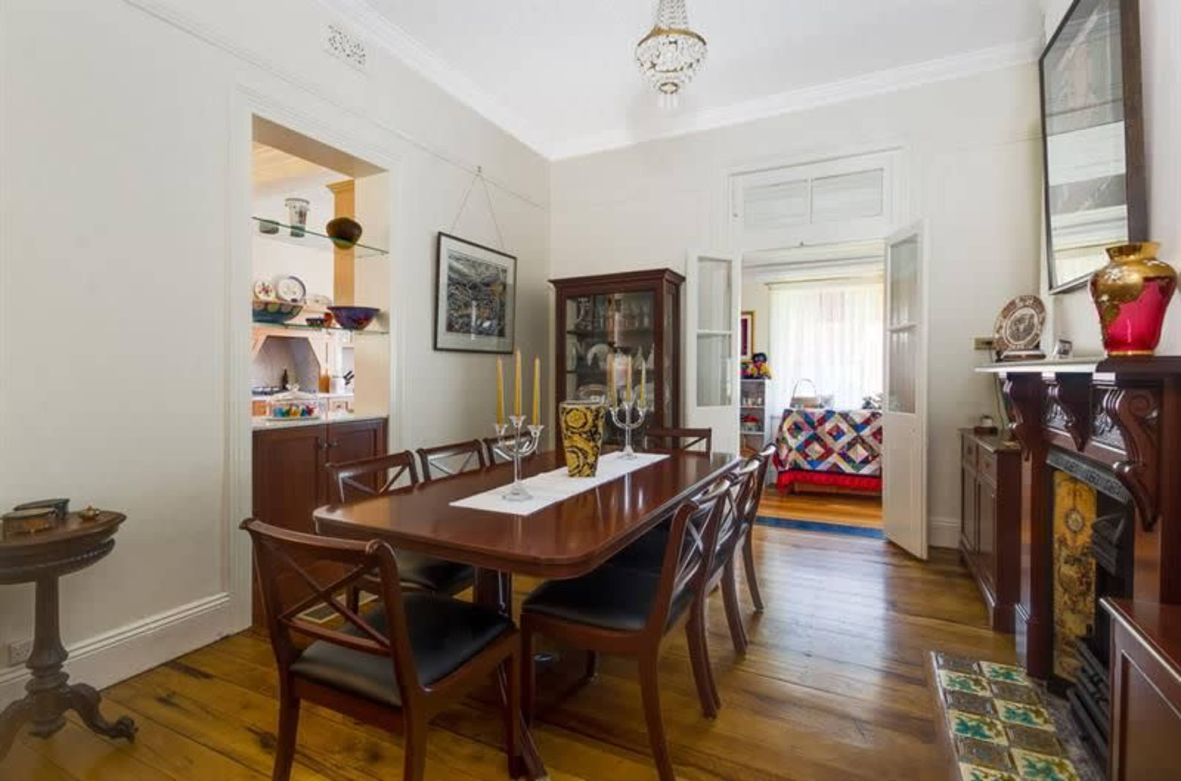 The image depicts a dining room with a wooden table surrounded by chairs, a china cabinet, and a fireplace, showcasing a blend of classic furnishings and decor.