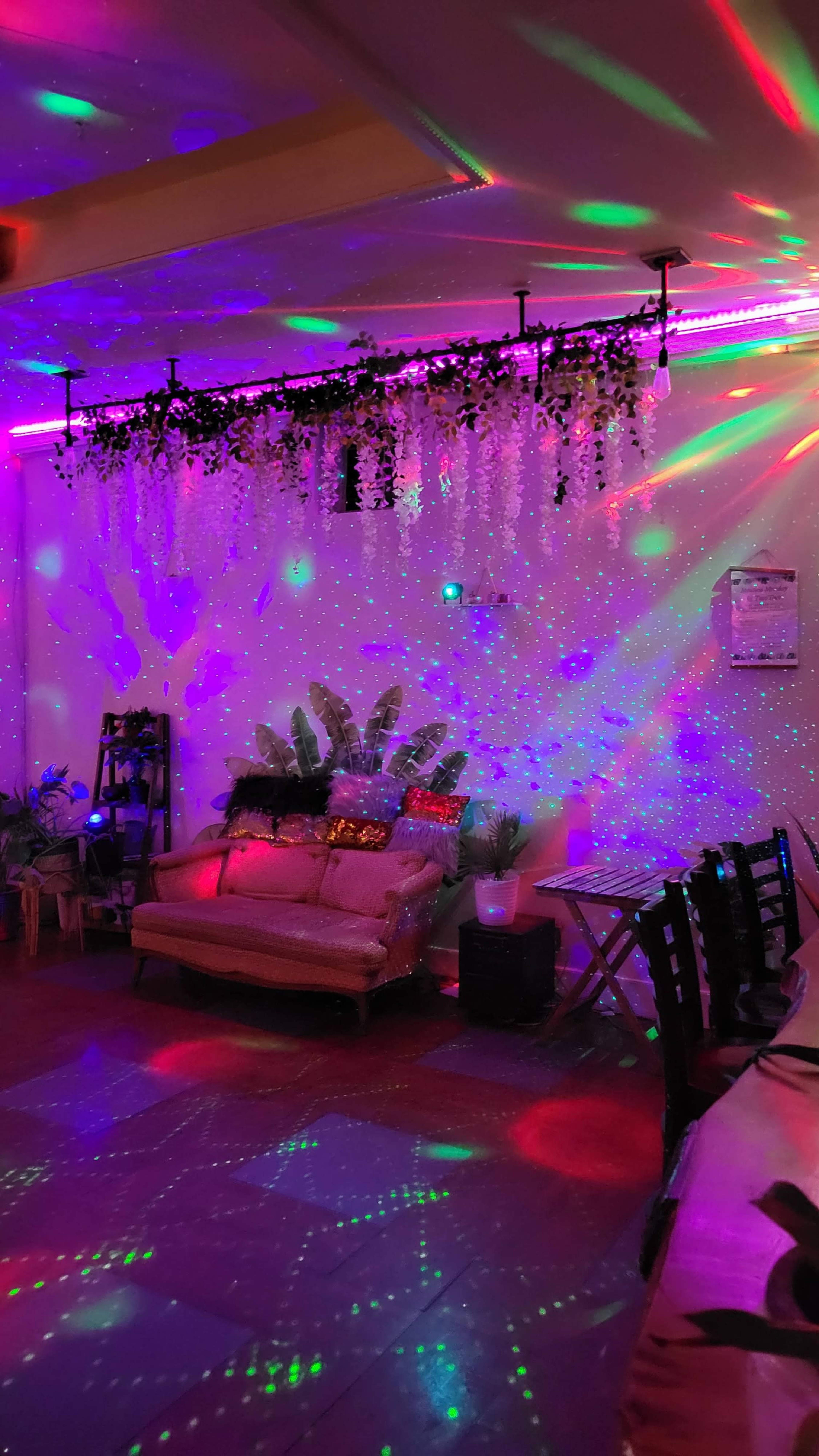 A brightly colored room with decorative lighting, a couch adorned with cushions, and plants arranged on the walls.